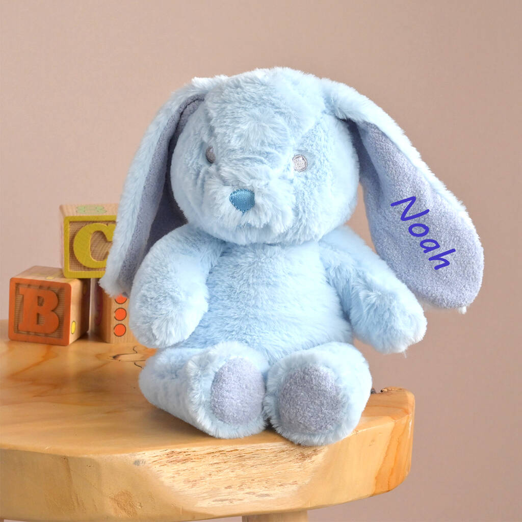 Blue bunny soft toy made from recycled fabric, personalised with the name Noah embroidered on one ear, sitting on a wooden stool next to alphabet blocks.