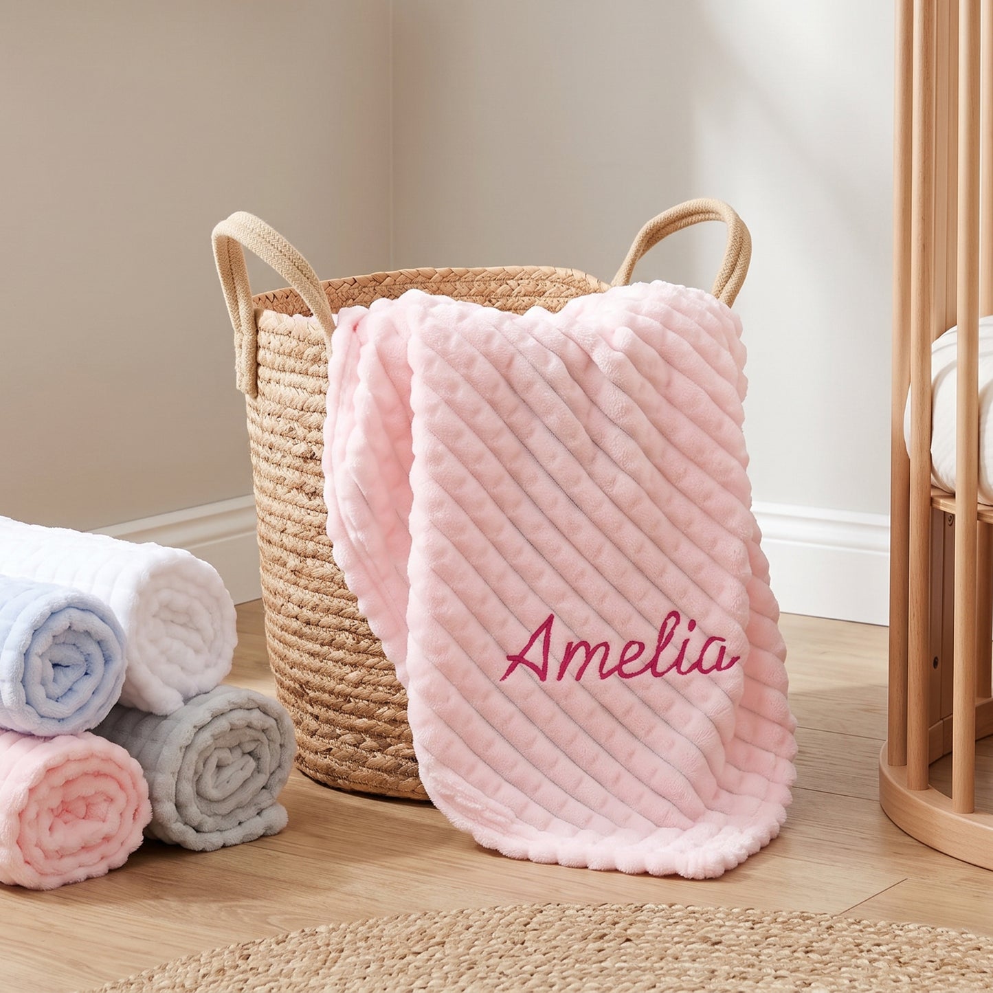 Pink ribbed fleece baby blanket personalised with the name Amelia, folded in a wicker basket with rolled yarn nearby.