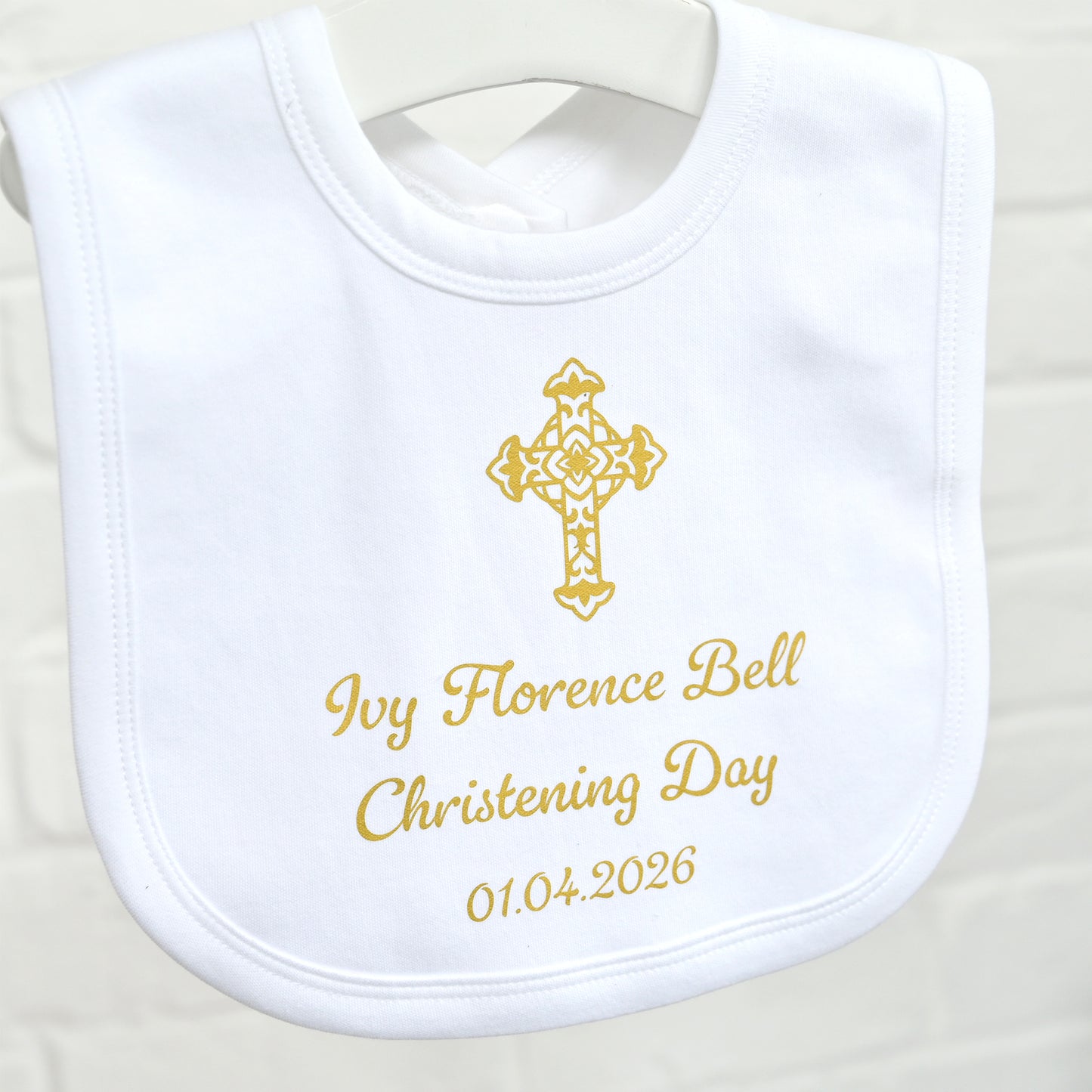 A white personalized baby bib with gold embroidered text reading 'Ivy Florence Bell Christening Day 01.04.