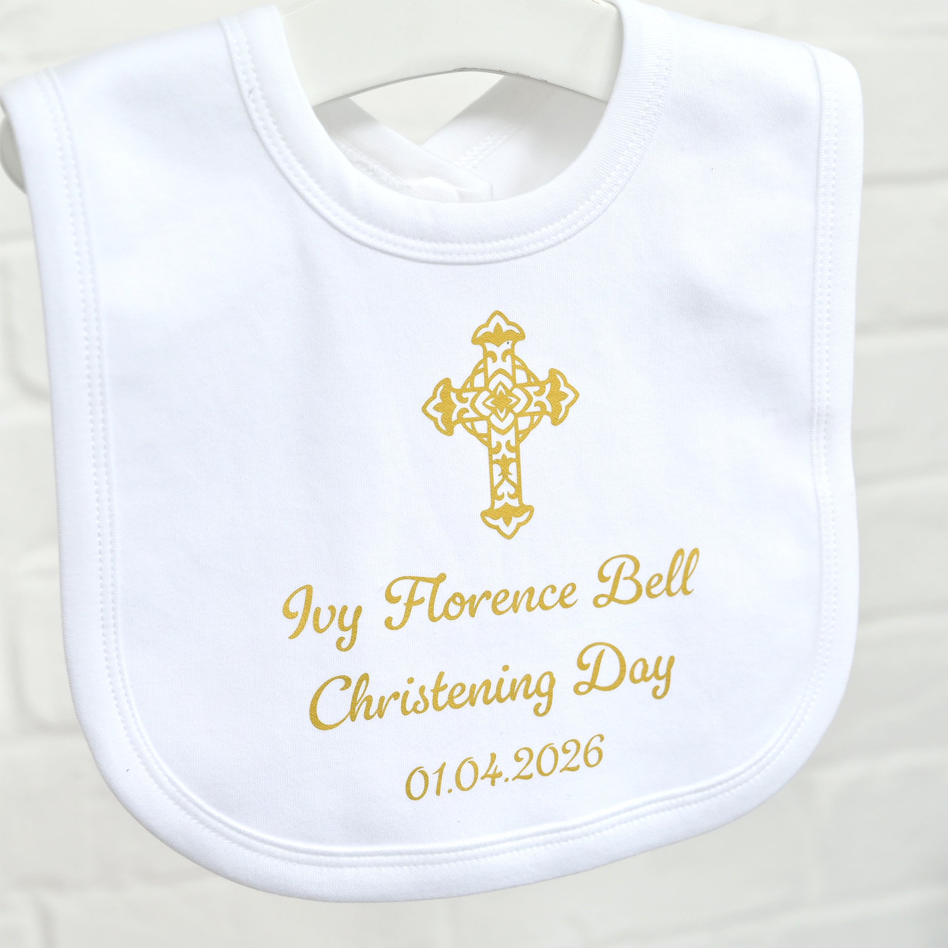 A white personalized baby bib with gold embroidered text reading 'Ivy Florence Bell Christening Day 01.04.