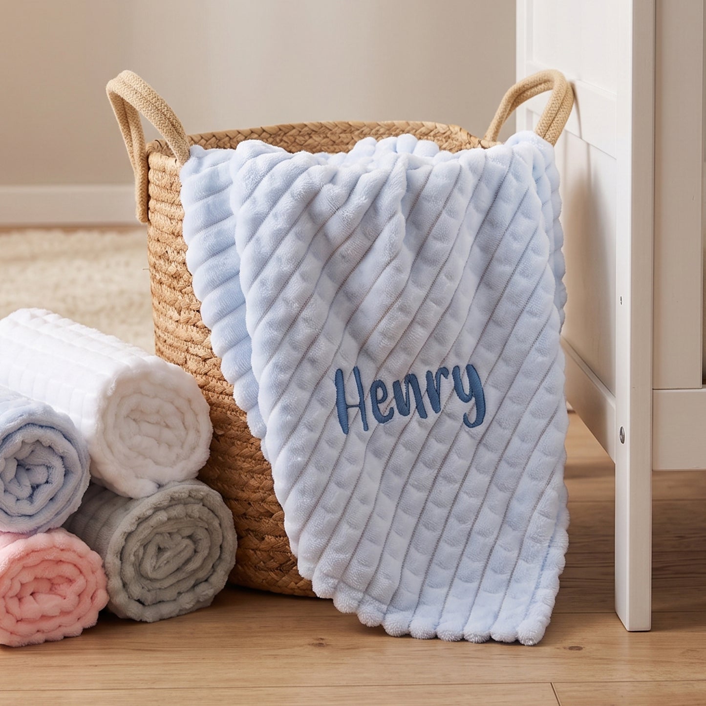 Blue ribbed fleece baby blanket personalised with the name Henry, folded in a wicker basket.