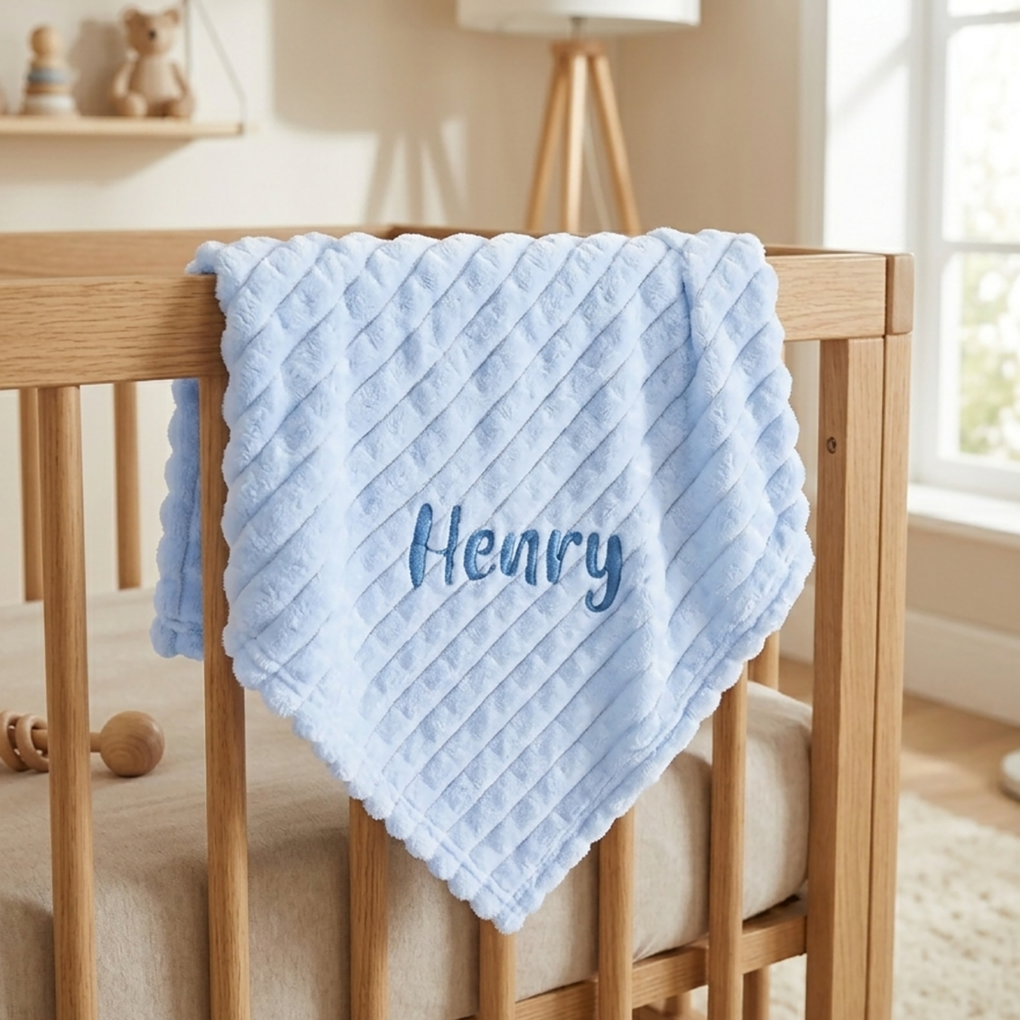 Blue ribbed fleece baby blanket hanging over a wooden crib rail, personalised with the name Henry.