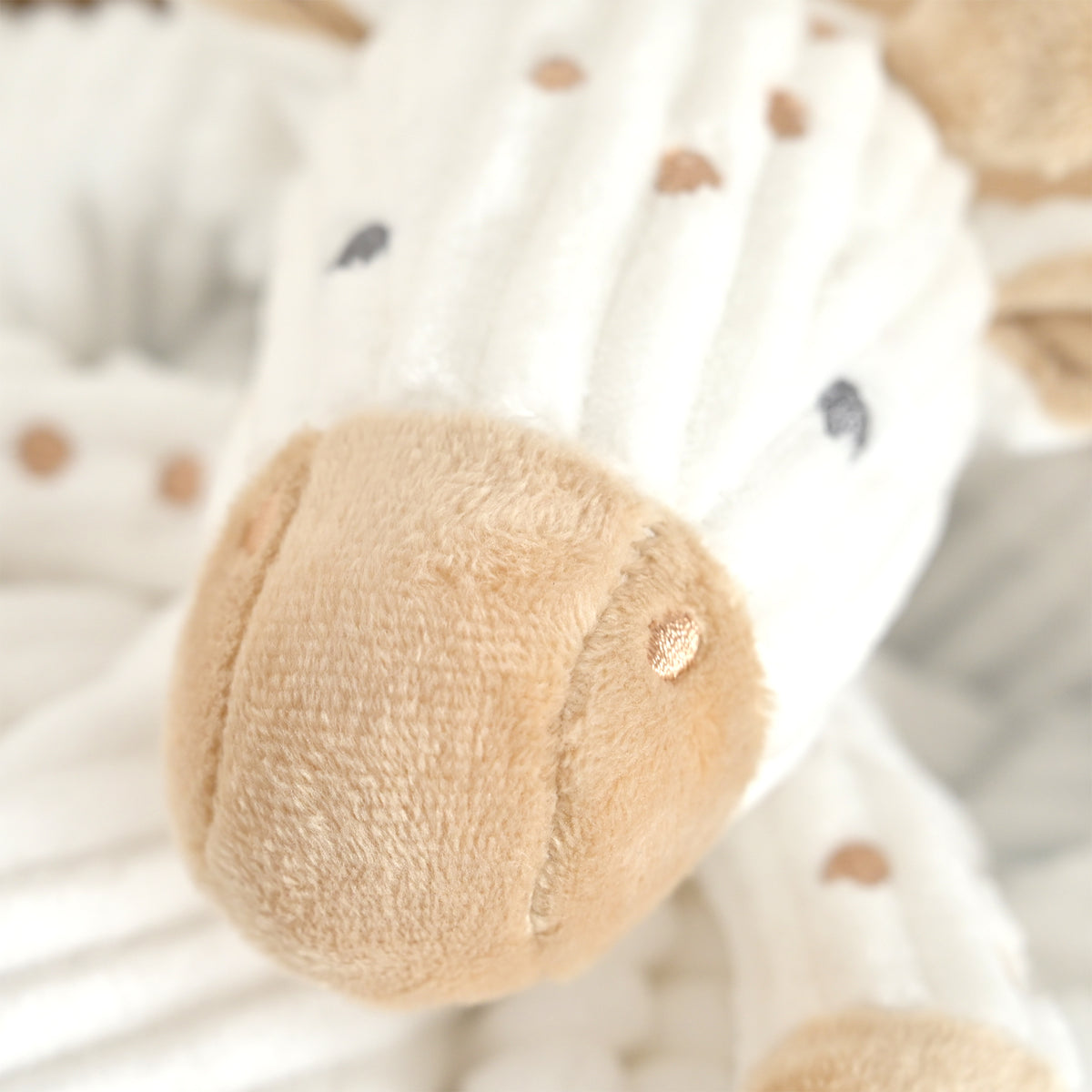 Close-up of a plush stuffed animal with a soft cream-white body, tan muzzle, and small tan and dark gray polka dots, photographed in a soft close-up view.