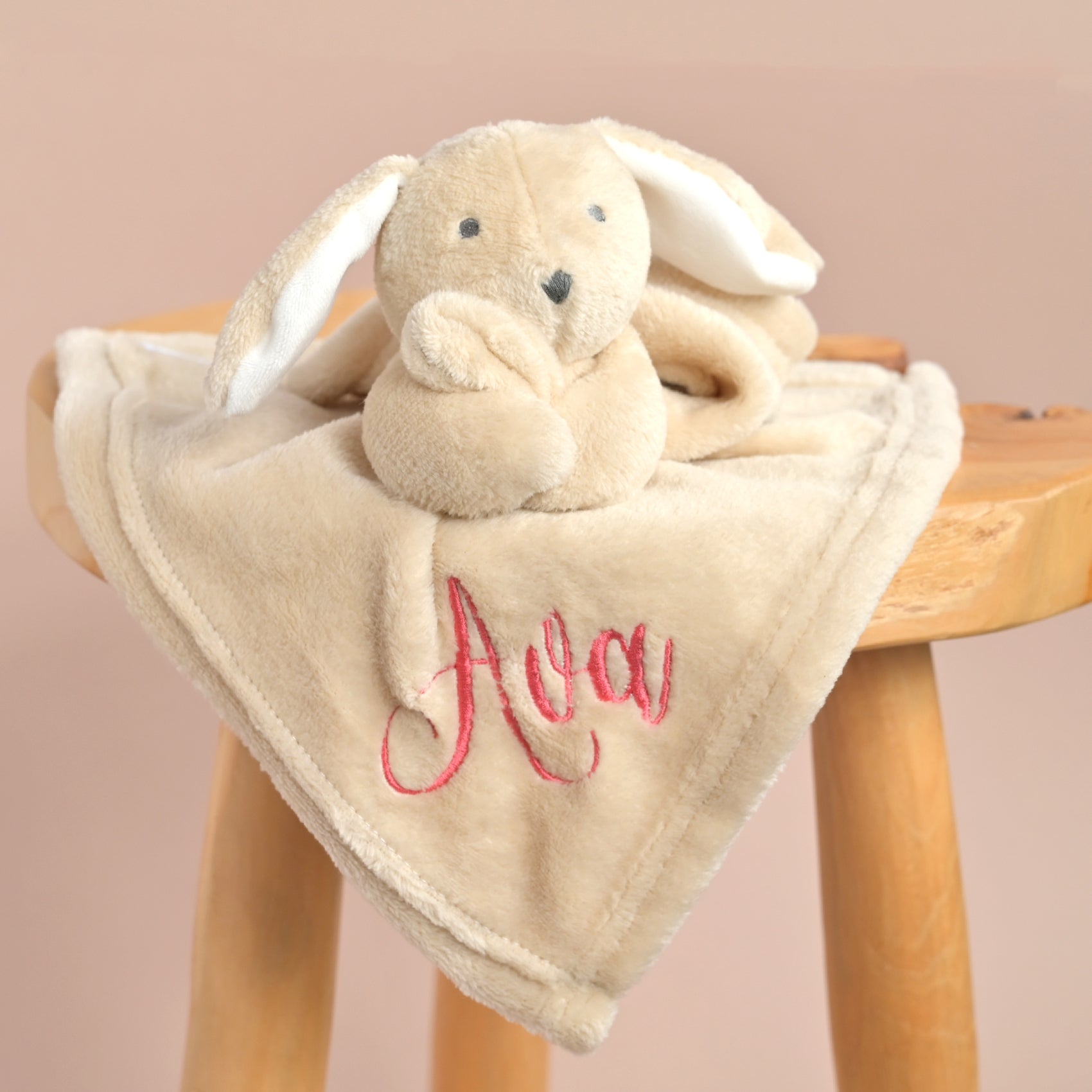 A beige plush bunny lovey blanket with a soft square corner, featuring the name 'Ava' embroidered in pink script on the front. The bunny has white inner ears and a small black stitched nose.