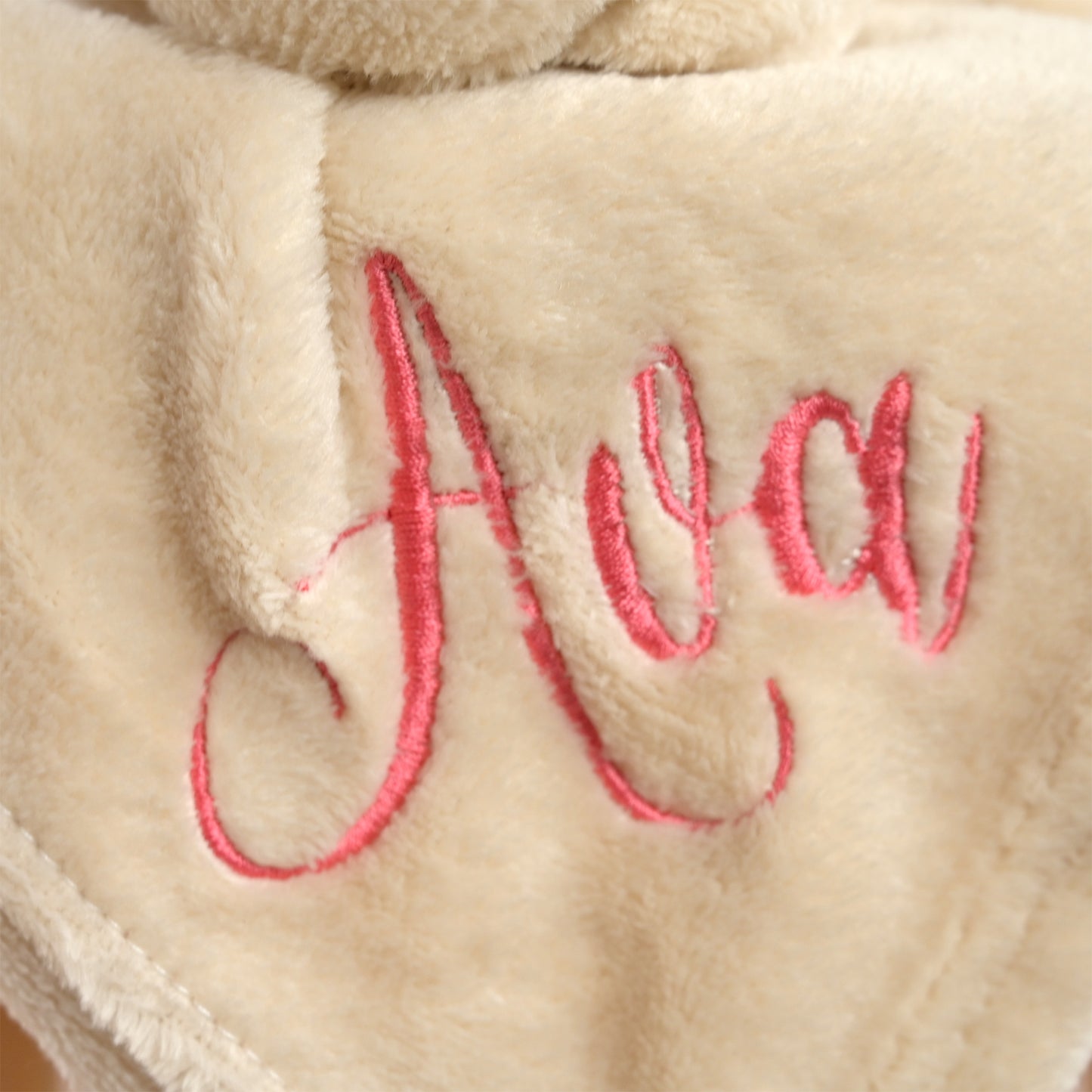 Close-up of a plush cream fleece blanket with pink embroidered cursive text reading 'Ava'.