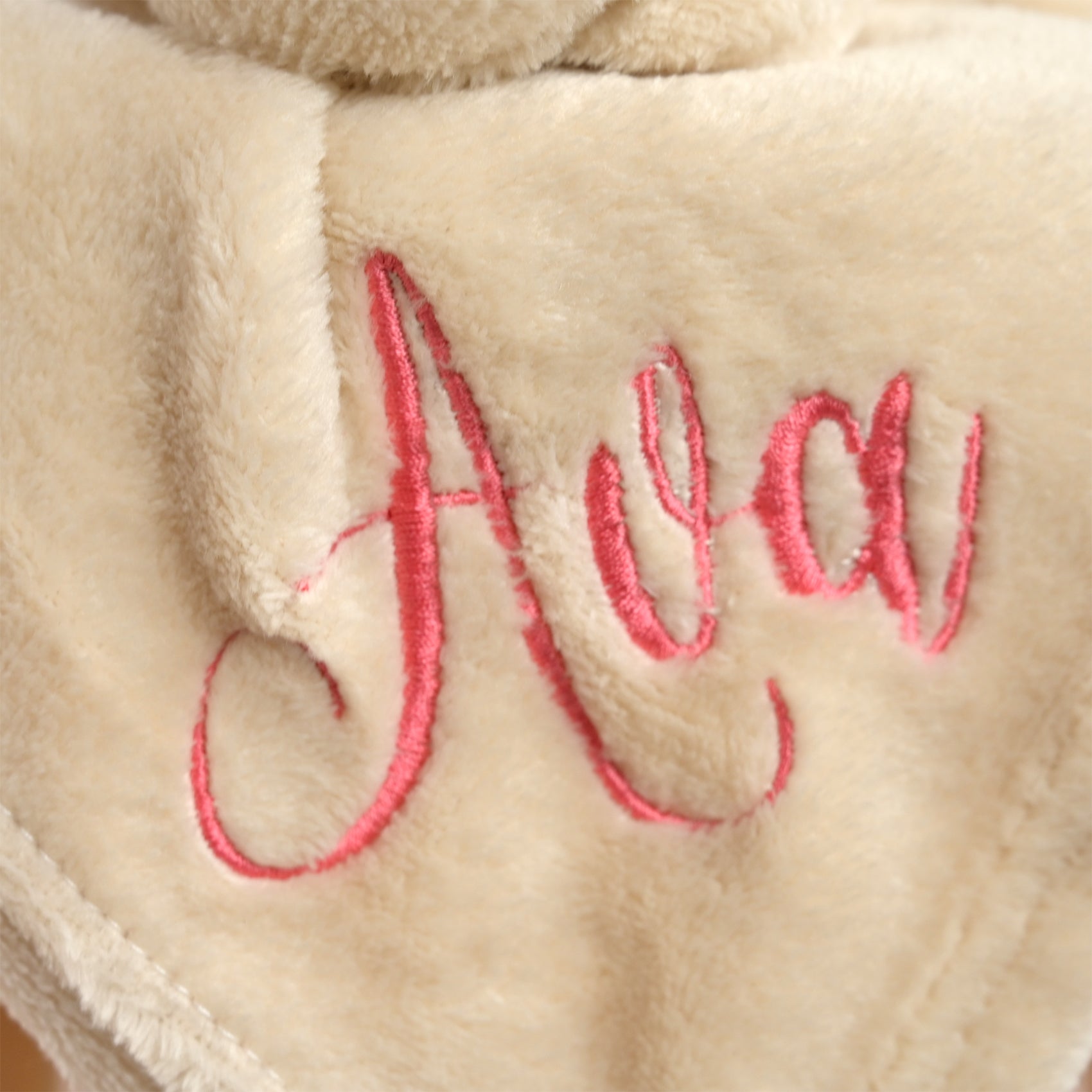Close-up of a plush cream fleece blanket with pink embroidered cursive text reading 'Ava'.