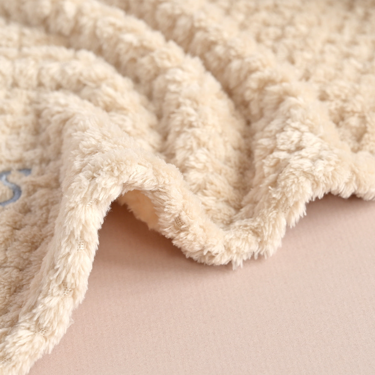 Close-up of a soft, plush cream-colored blanket with a textured sherpa or fleece surface draped over a light beige surface.