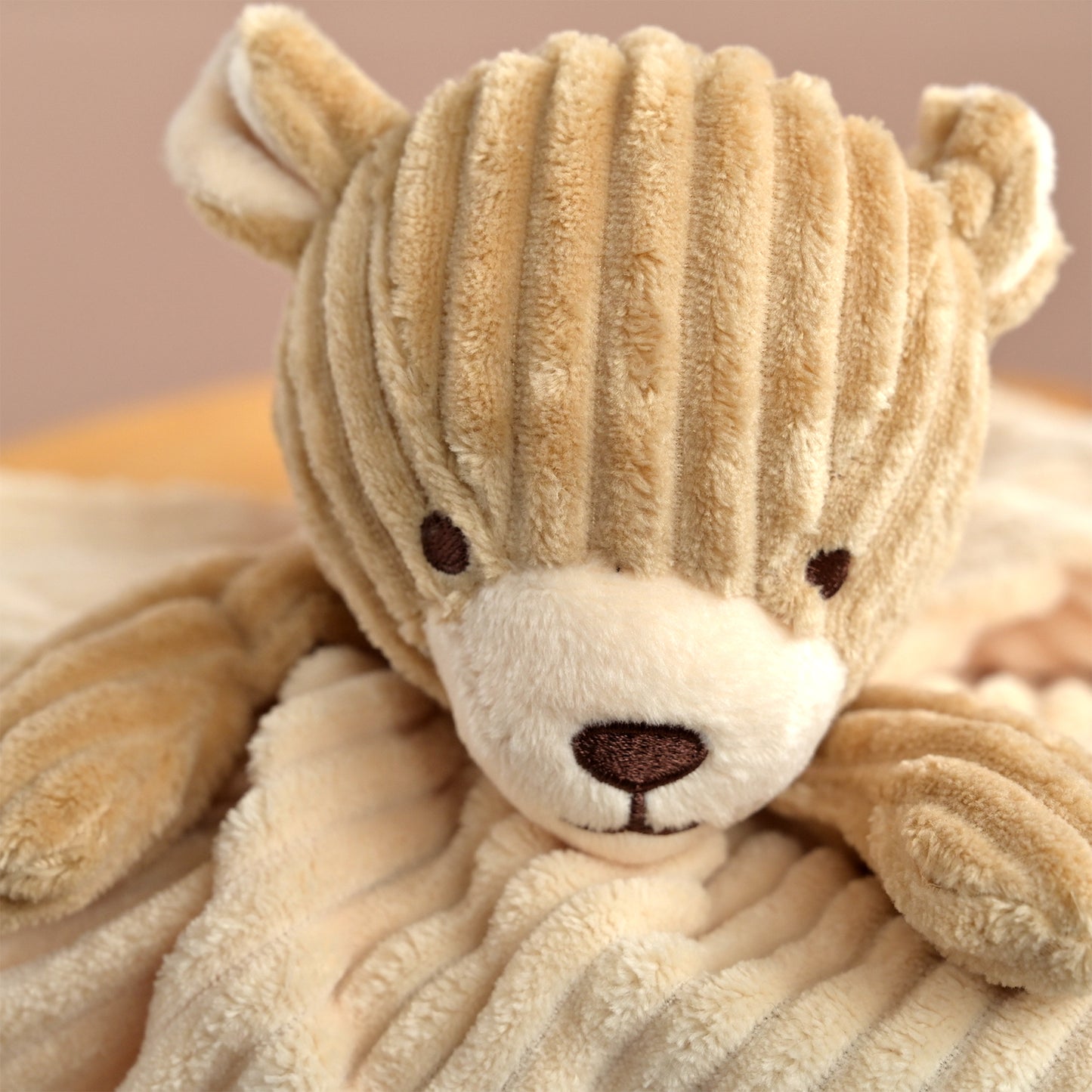 A close-up of a teddy bear security blanket featuring a beige corduroy bear head and a soft cream plush body, resting on a neutral background.