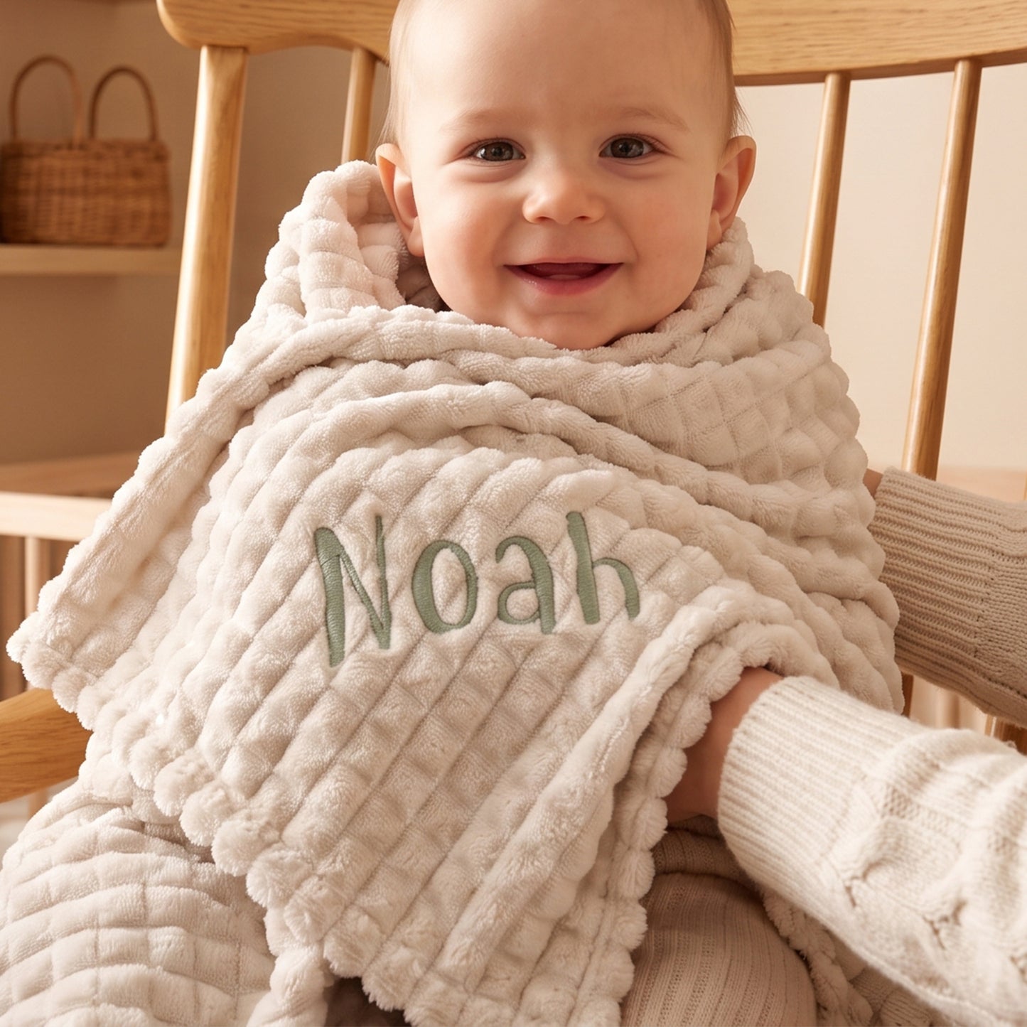 Coffee ribbed fleece baby blanket personalised with the name Noah in sage green embroidery, wrapped around a baby sitting in a wooden chair.