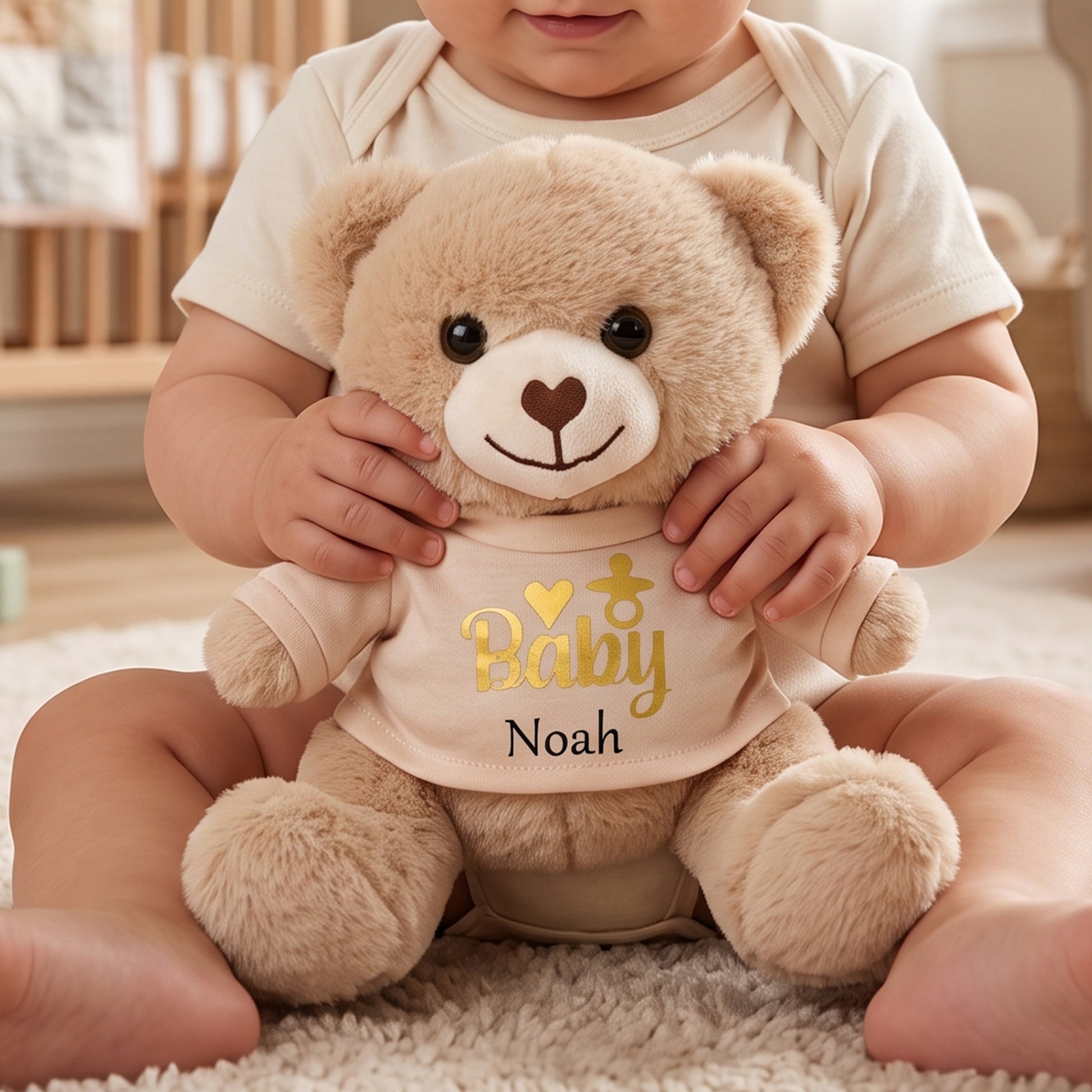 Tan teddy bear soft toy wearing a tan t-shirt printed with "Baby" in gold and a dummy icon, personalised with the name Noah, held by a baby.