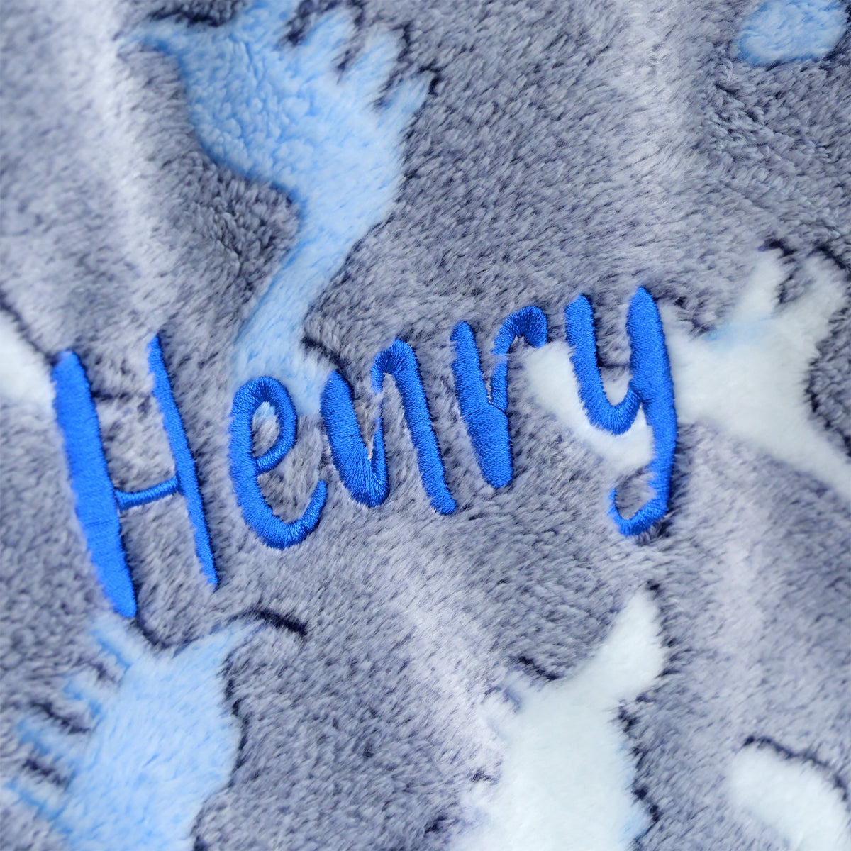 Close-up of a plush fleece blanket with the name 'Henry' embroidered in bright blue script over a gray and white cloud pattern.