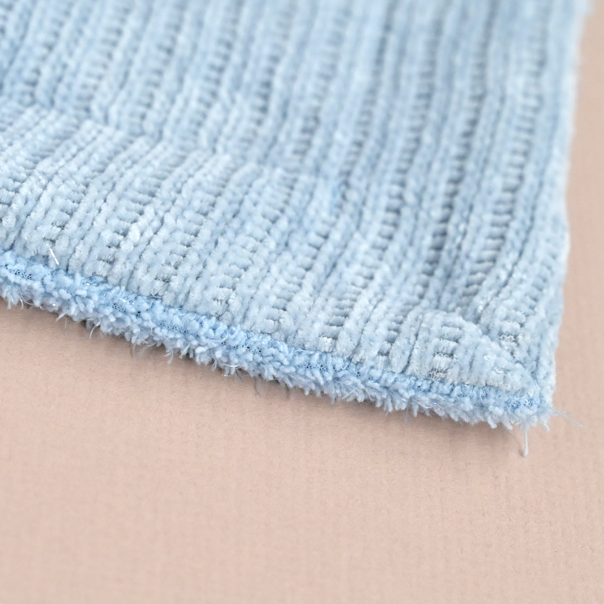 A close-up of a light blue textured woven fabric corner with a frayed edge, laid against a plain beige background.