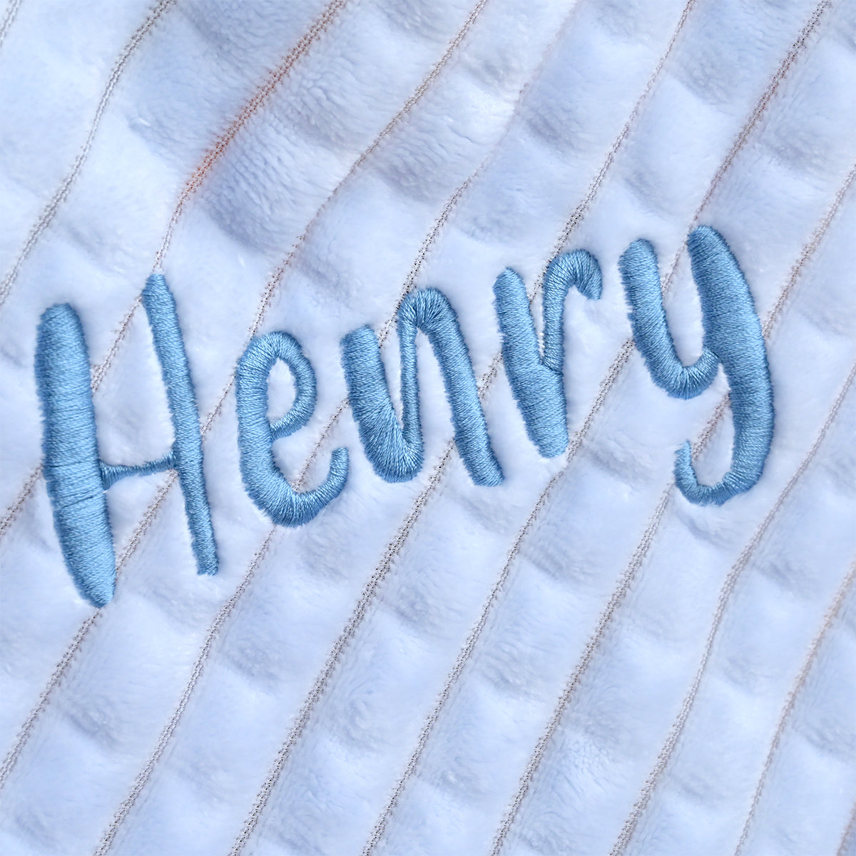 Close-up of the name Henry embroidered in navy blue thread on light blue ribbed fleece fabric.