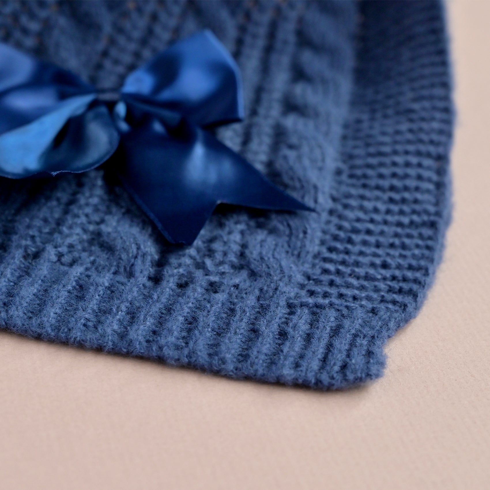 Close-up of a navy satin bow stitched onto cable knit baby blanket fabric.