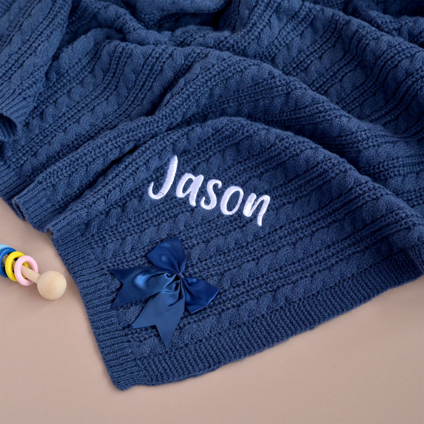 Navy cable knit baby blanket laid flat showing the embroidered name Jason and satin bow in full.