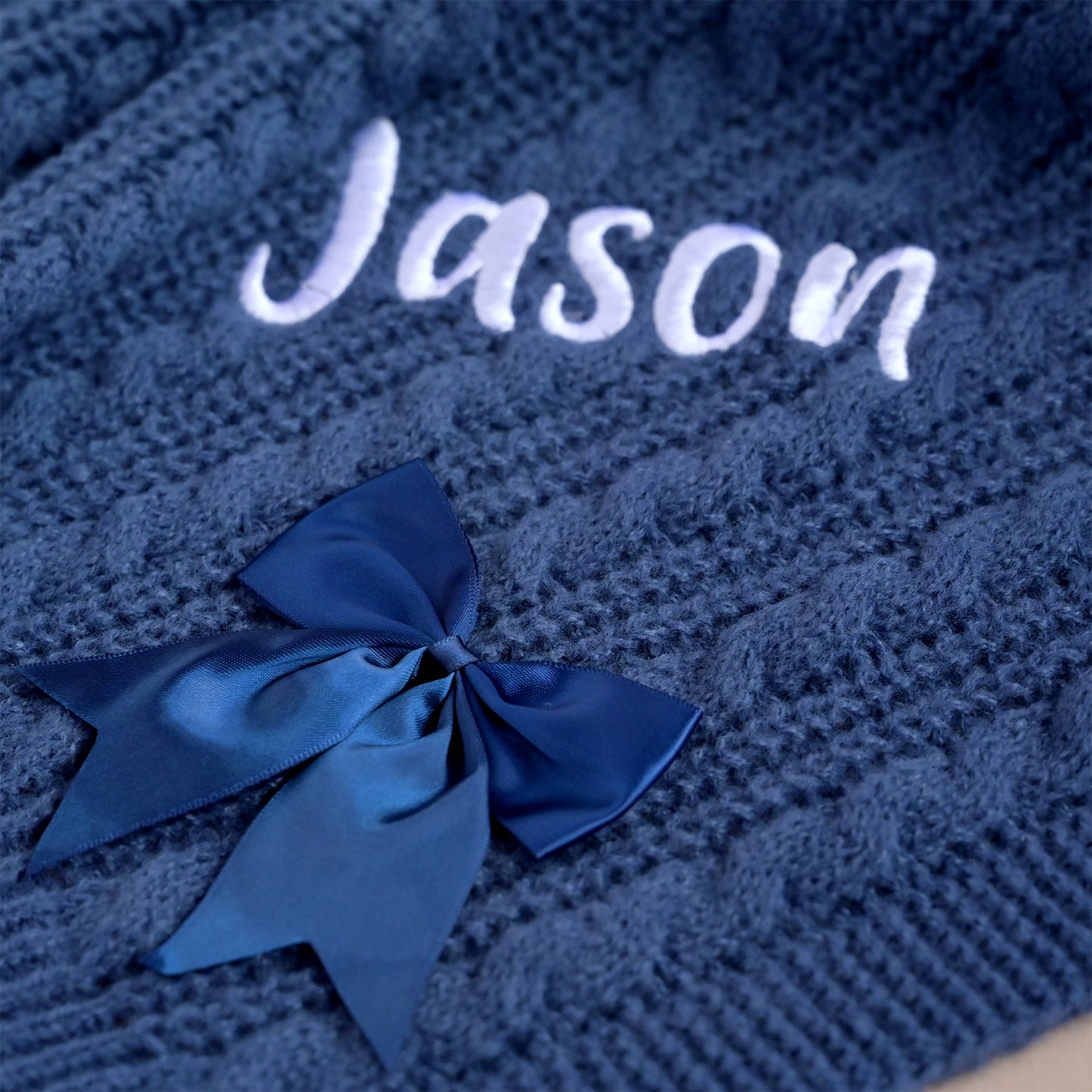 Corner of a navy cable knit baby blanket showing the embroidered name Jason in white thread.