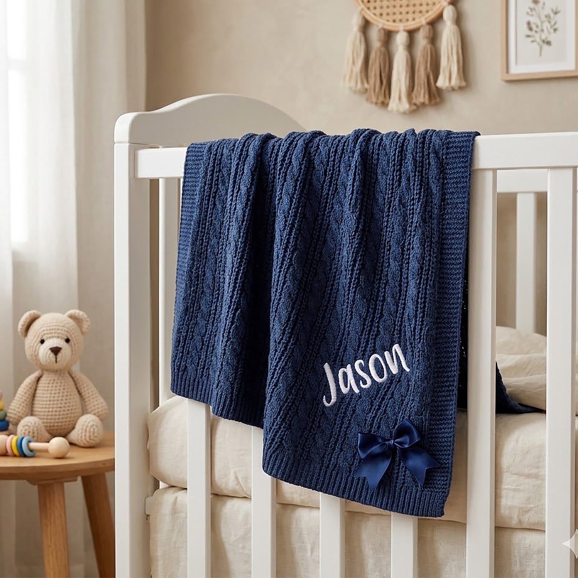 Navy cable knit baby blanket hanging over a wooden crib rail, personalised with the name Jason and a navy satin bow.