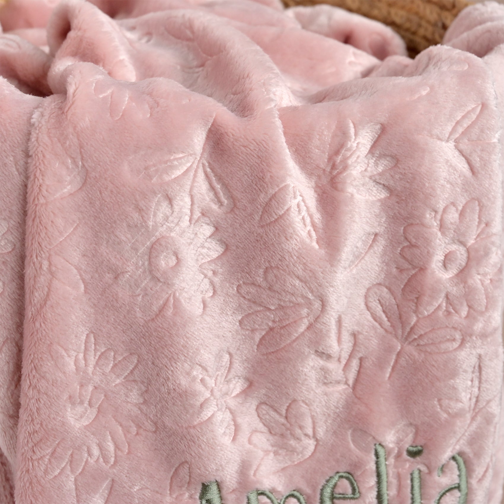 A close-up of a soft pink plush blanket with an embossed floral pattern and the name 'Amelia' embroidered in green at the bottom.