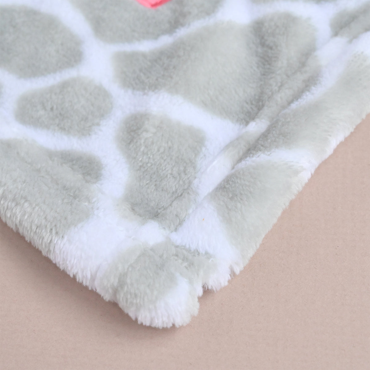 A close-up of a plush fleece blanket with a light gray and white giraffe-like pattern, folded over to show its soft texture on a plain beige background.