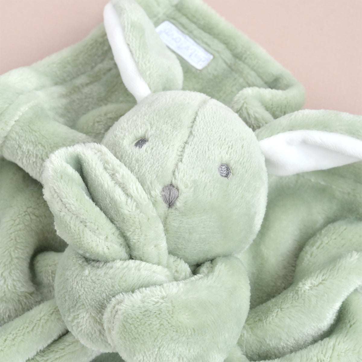 A close-up of a plush bunny comforter or blanket in soft sage green, showing the stuffed bunny face and ears attached to a matching plush fabric cover with white inner-ear details.