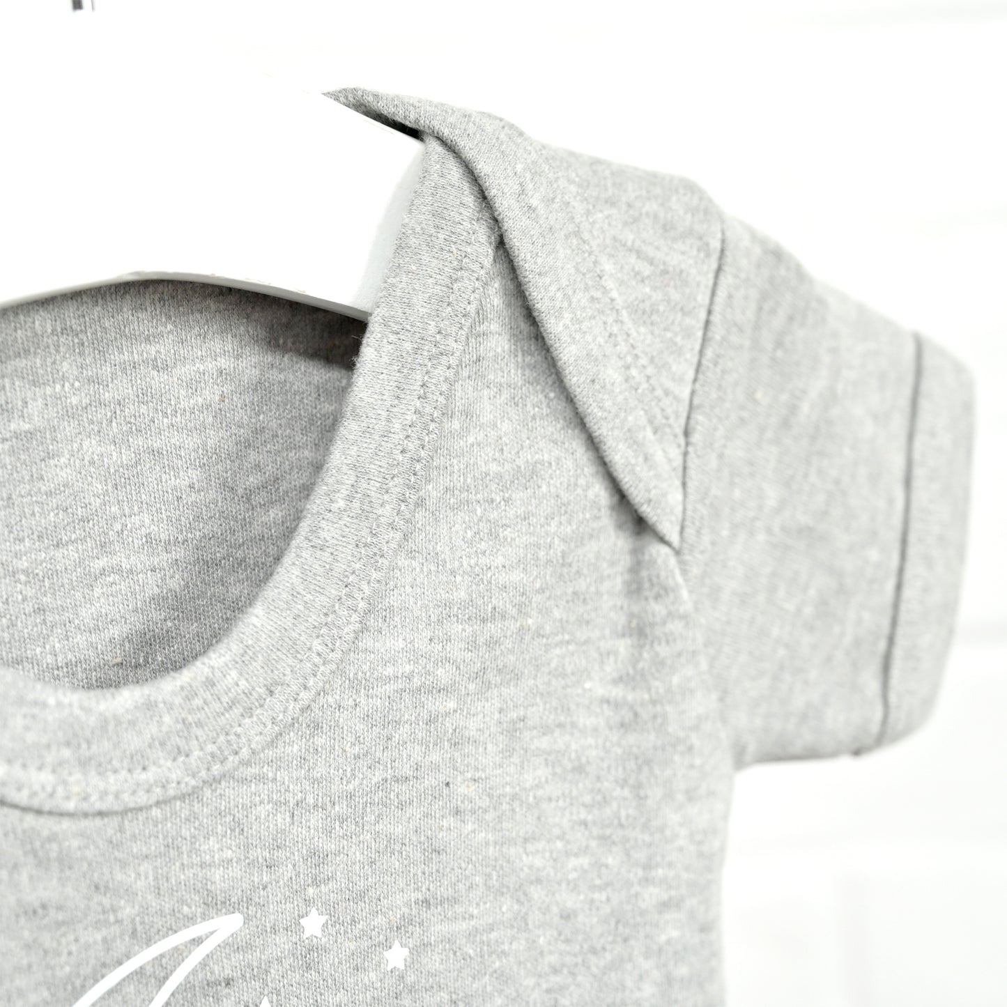 Close-up of a light heather gray short-sleeve baby t-shirt on a white hanger, showing the crew neck and a small white crescent moon and star graphic on the chest.