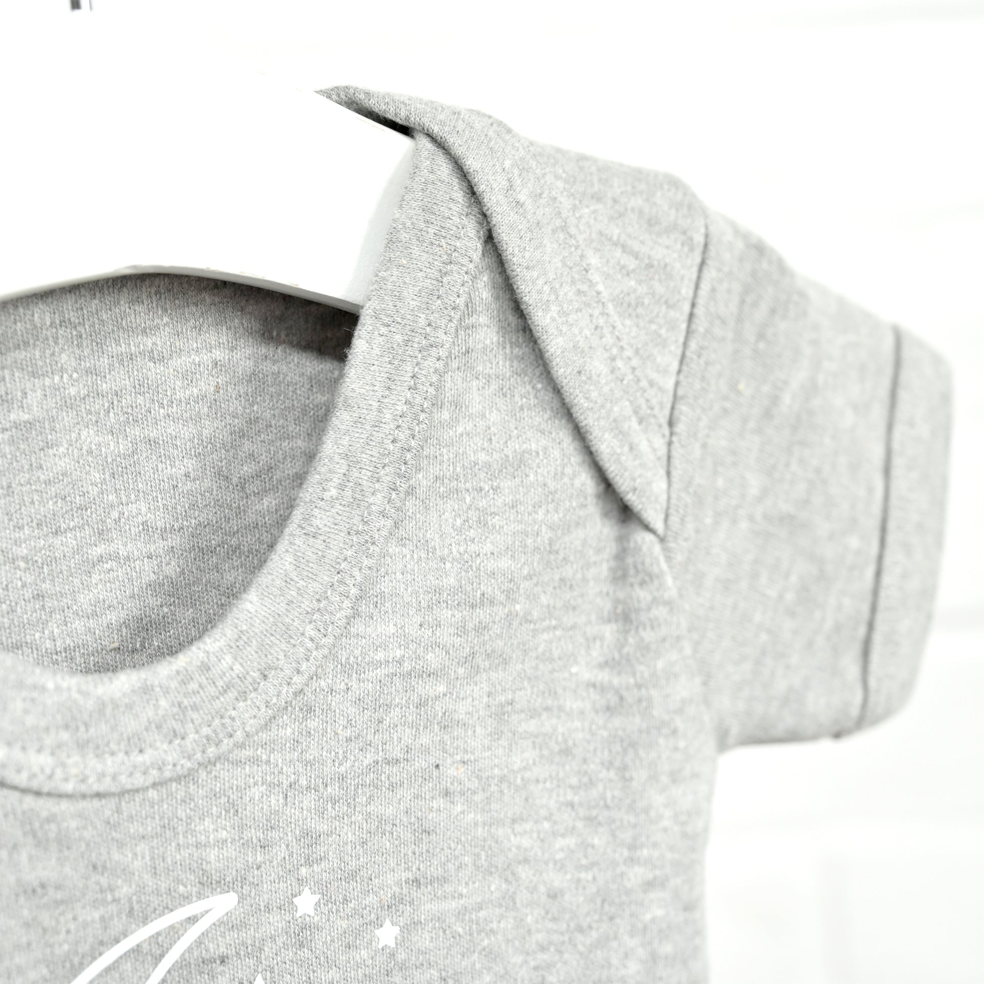 Close-up of a light heather gray short-sleeve baby t-shirt on a white hanger, showing the crew neck and a small white crescent moon and star graphic on the chest.
