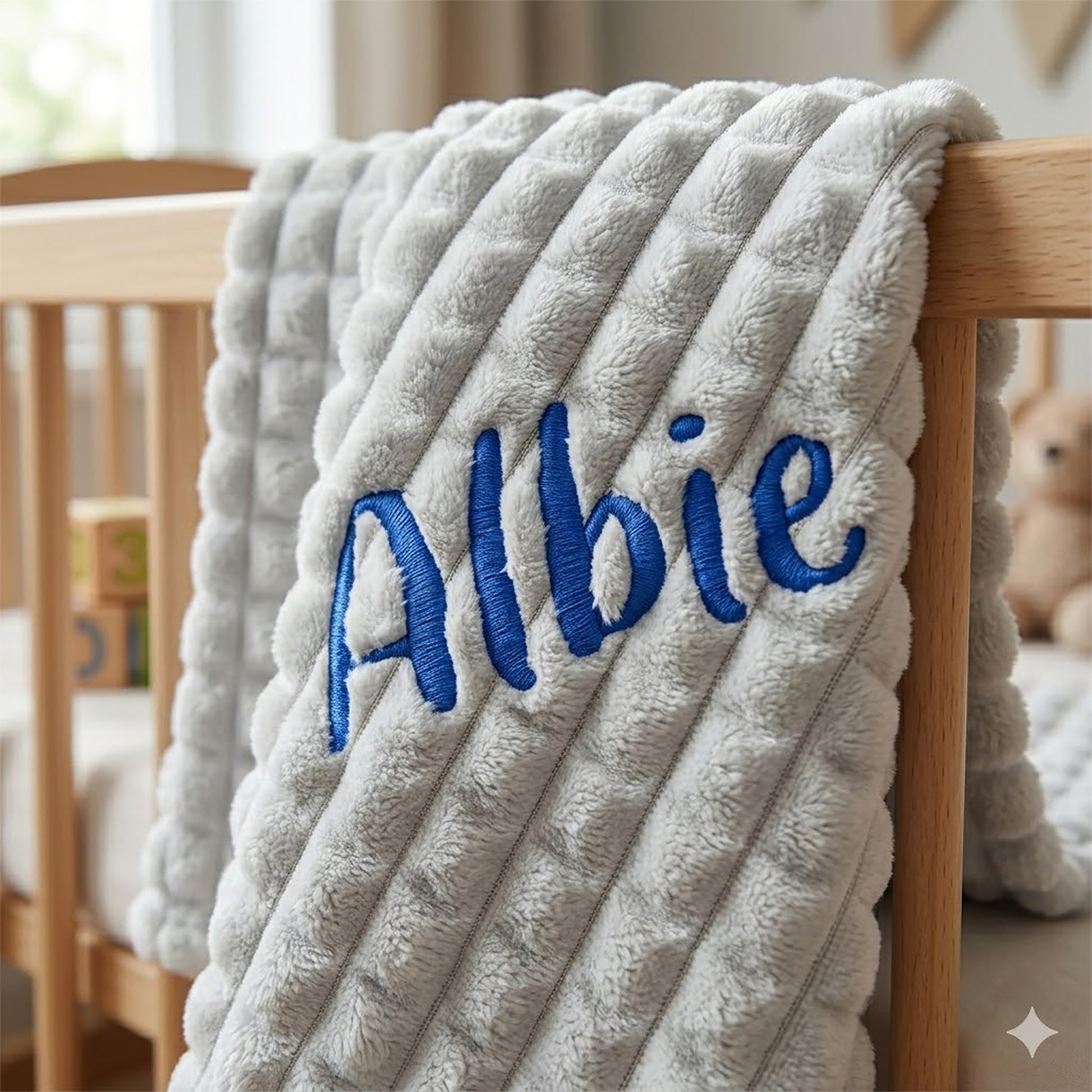 A close-up of a plush ribbed baby blanket draped over a wooden crib, personalized with the name 'Albie' in blue embroidered script.
