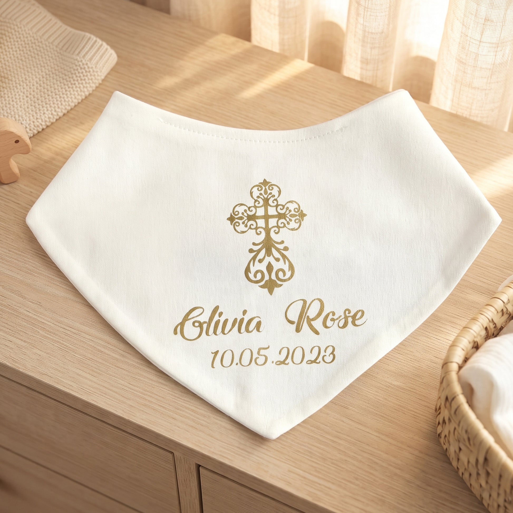 A white baby bib with a gold cross design and personalized text reading 'Elvia Rose 10.05.