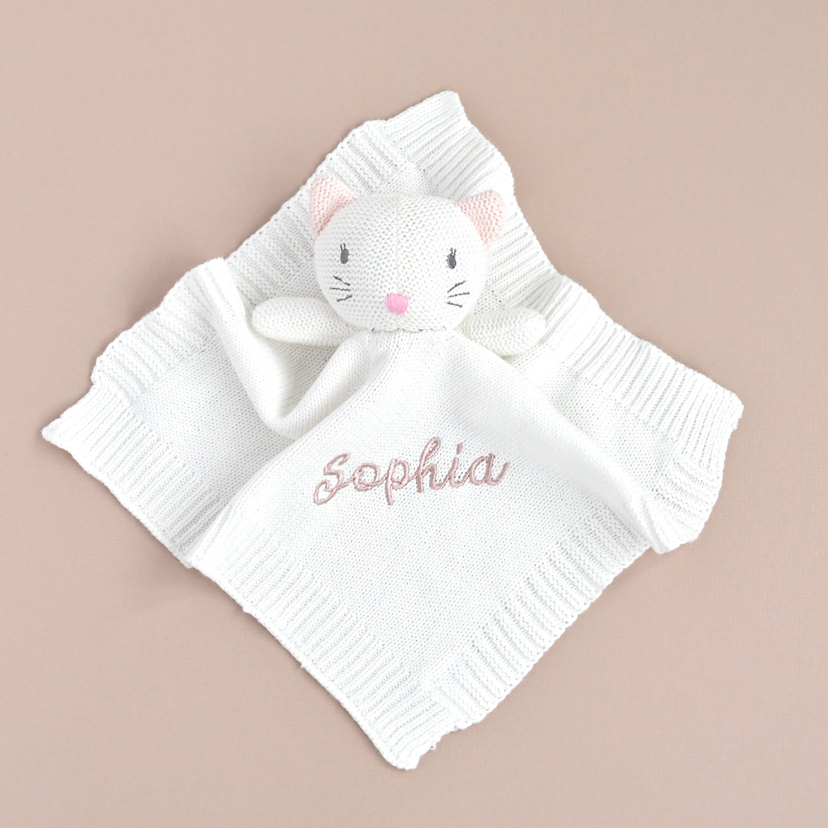 A white knitted baby lovey blanket featuring a plush cat head with pink ears and nose, and the name 'Sophia' embroidered in pink script on the front, displayed on a solid beige background.