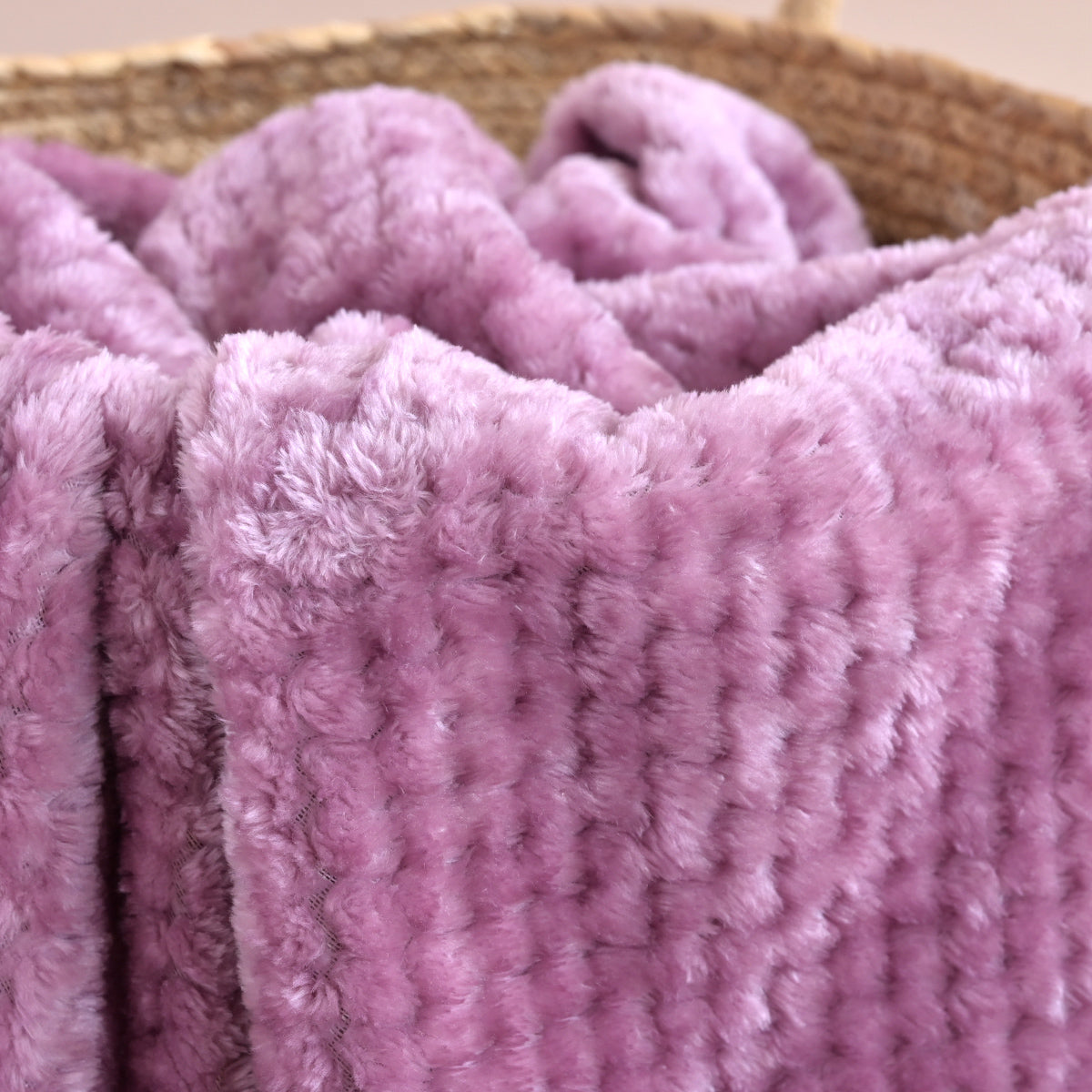 A close-up of a plush, textured lavender-purple blanket draped over a woven basket.