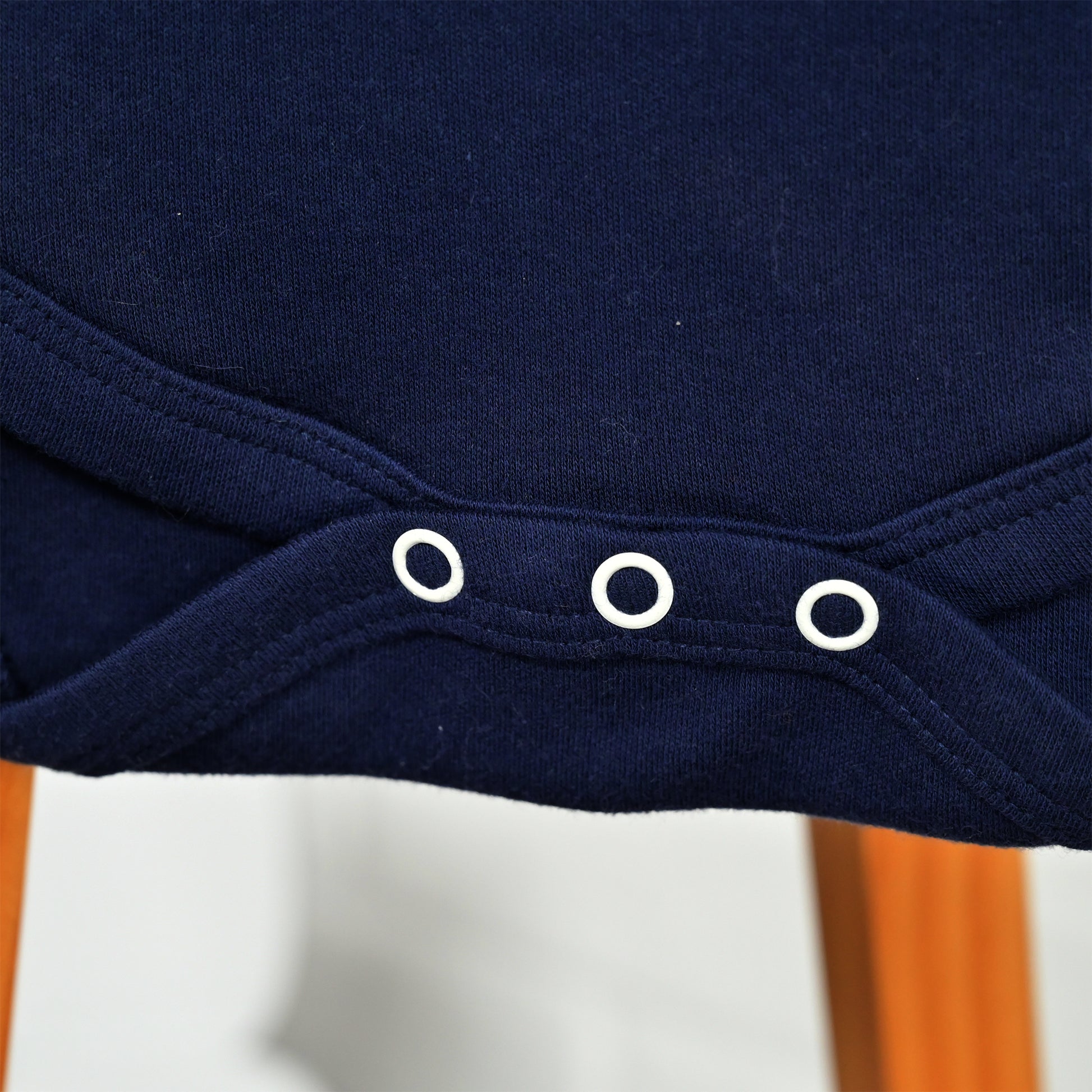 Close-up of a navy blue garment with three white eyelet snaps along a curved hem, shown against a softly blurred indoor background.
