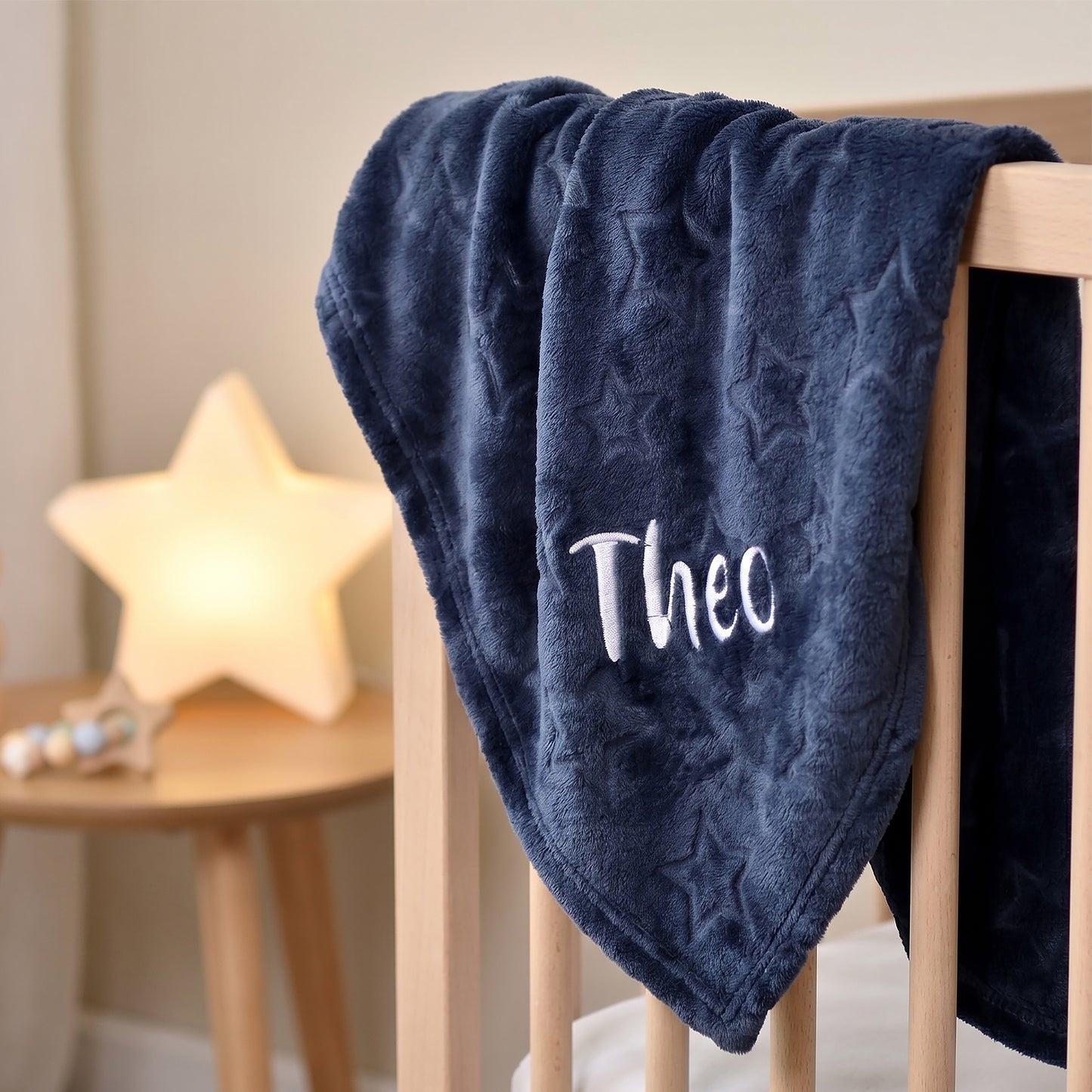 Navy blue textured blanket with 'Theo' embroidered on it, draped over a wooden crib.