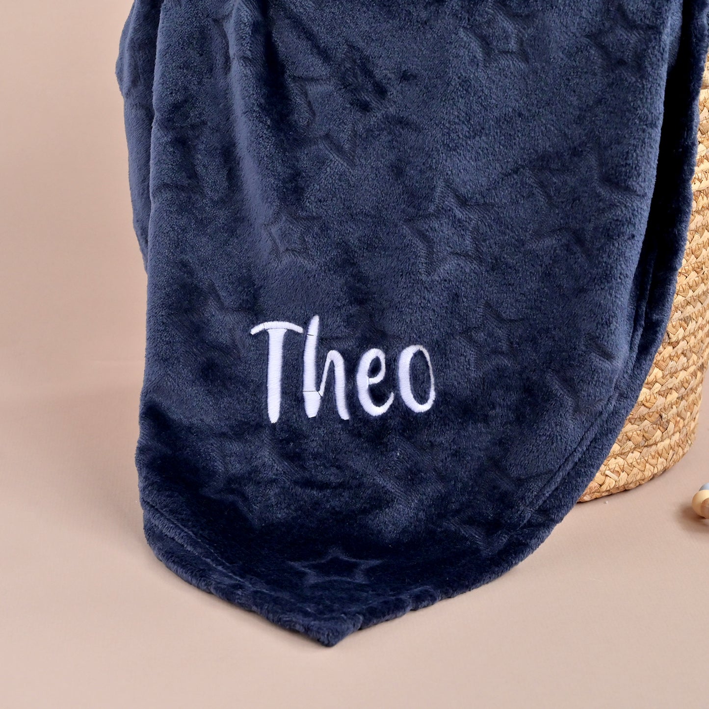 Navy blue blanket with 'Theo' embroidered on it, placed on a beige surface.