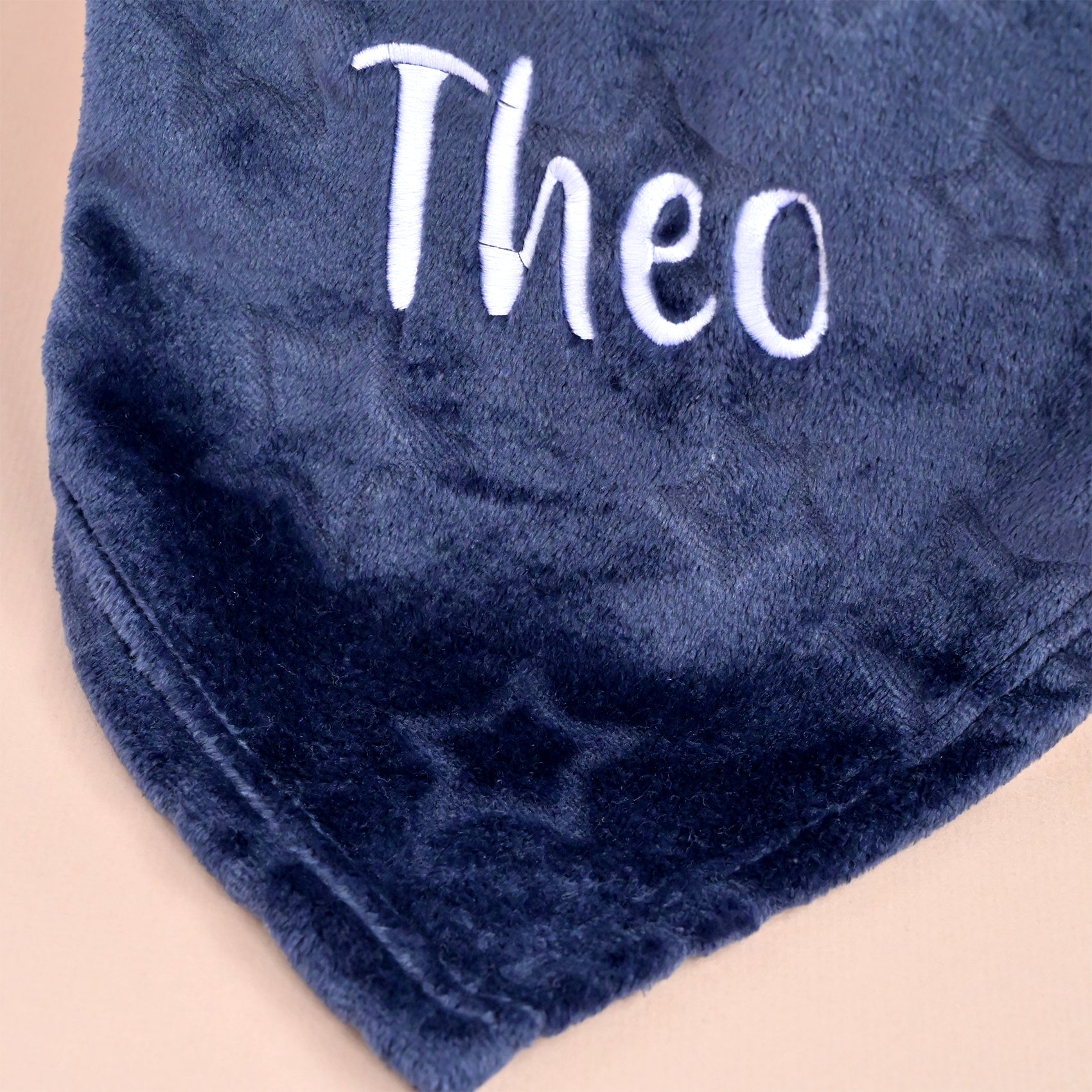 Close-up of the name Theo embroidered in white thread on navy embossed star fleece fabric.