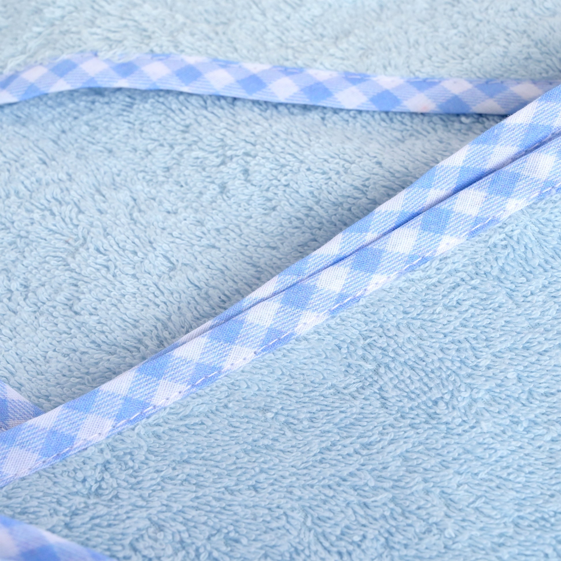 A close-up of a light blue terry cloth fabric with a diagonal light blue and white gingham ribbon trim.