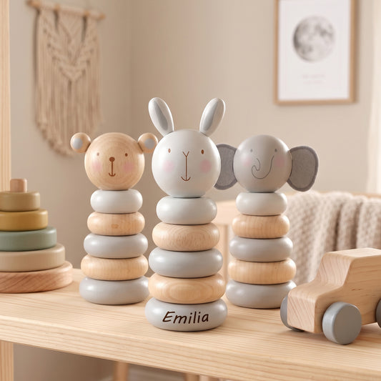 Three personalized wooden stacking toy animals (bear, rabbit, elephant) with the name 'Emilia' engraved on the rabbit's base, displayed on a light wood shelf in a cozy nursery setting.