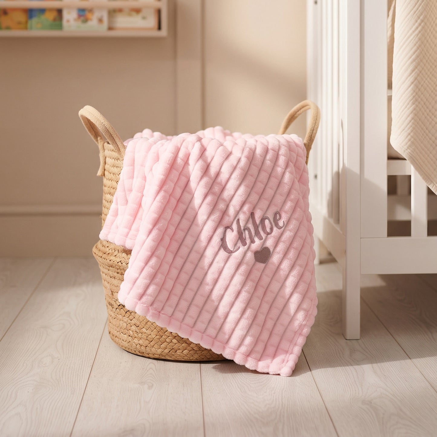 Pink ribbed fleece baby blanket personalised with the name Chloe and a small embroidered heart, draped over a woven basket.