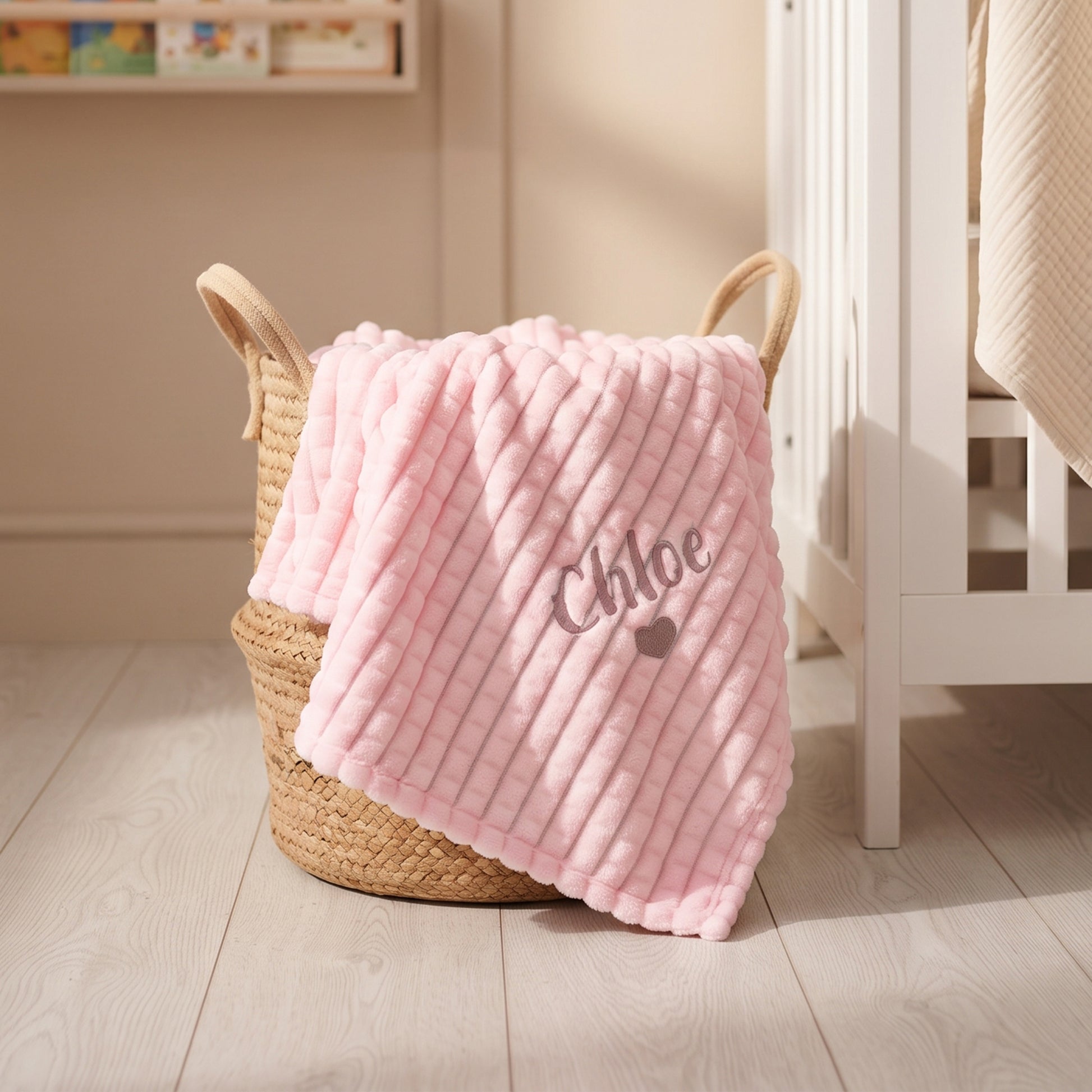 Pink ribbed fleece baby blanket personalised with the name Chloe and a small embroidered heart, draped over a woven basket.