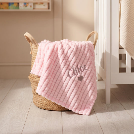 Pink ribbed fleece baby blanket personalised with the name Chloe and a small embroidered heart, draped over a woven basket.
