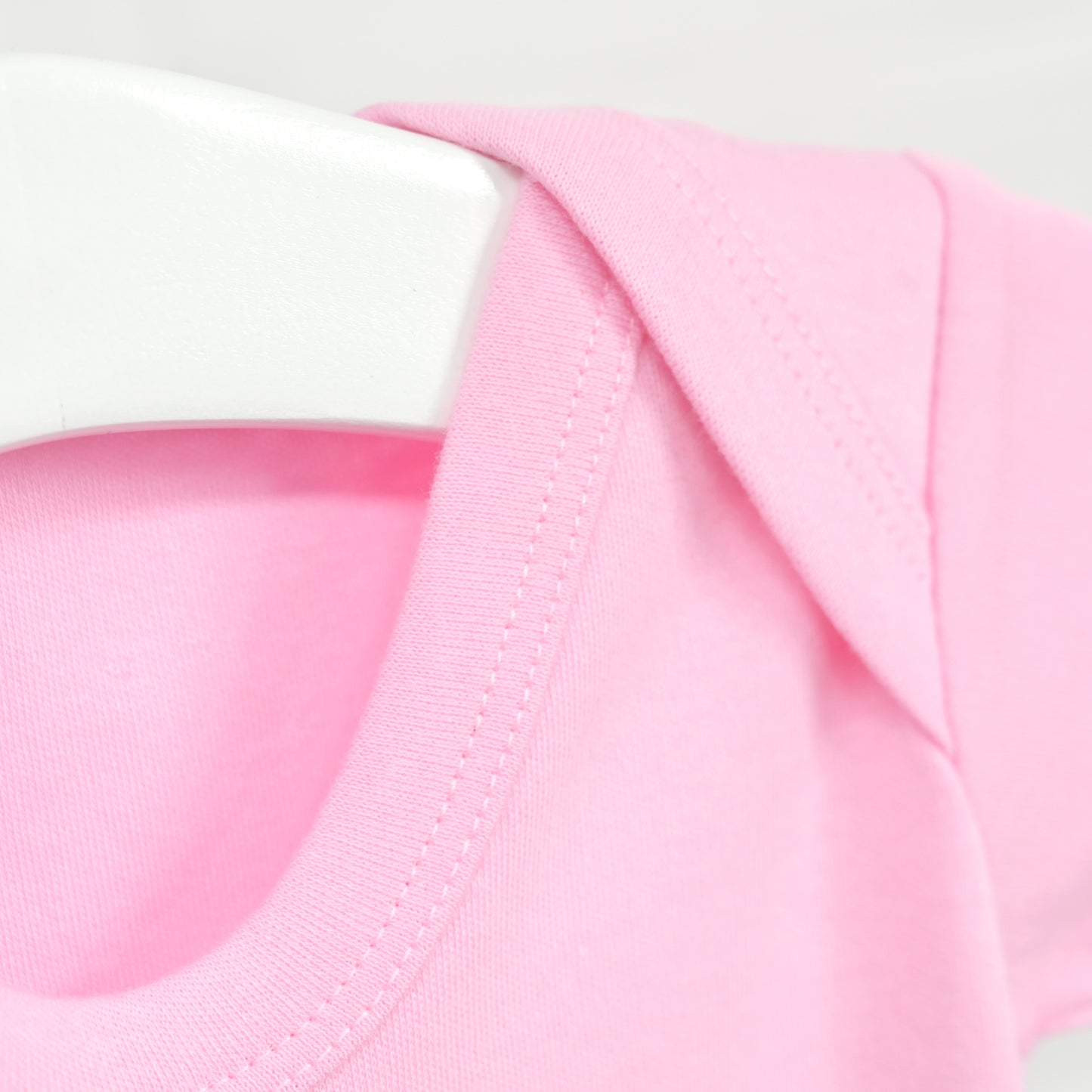 Close-up of a light pink crew-neck garment, likely a baby bodysuit or t-shirt, shown on a white hanger against a white background.