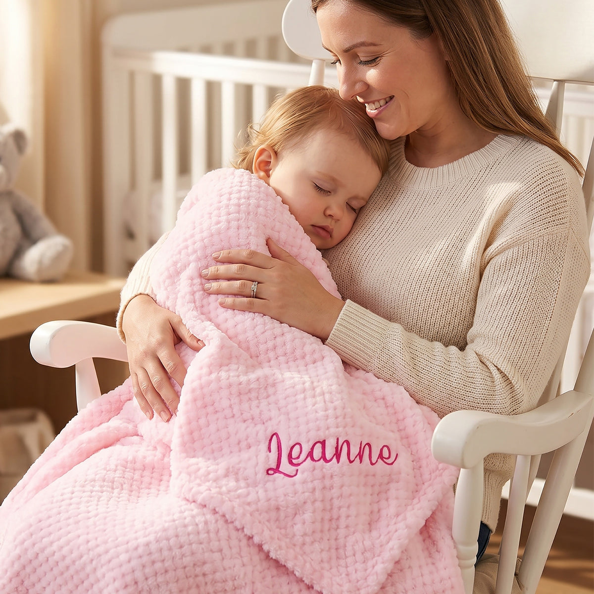 Pink waffle-knit baby blanket personalised with the name Leanne in pink script, wrapped around a smiling baby held by her mother.