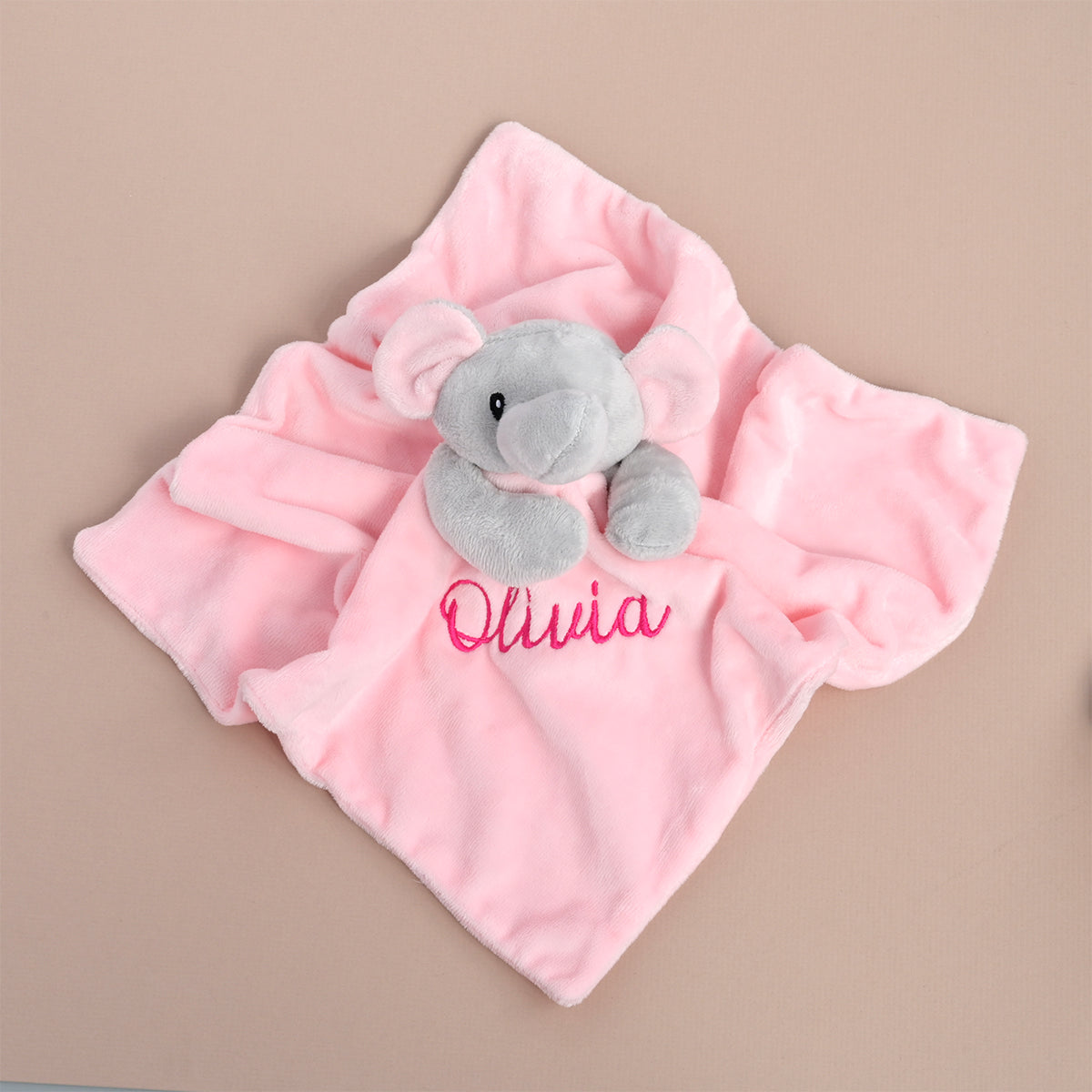 A pink plush baby security blanket featuring a small gray elephant toy and the name 'Olivia' embroidered in pink script, displayed on a solid beige background.