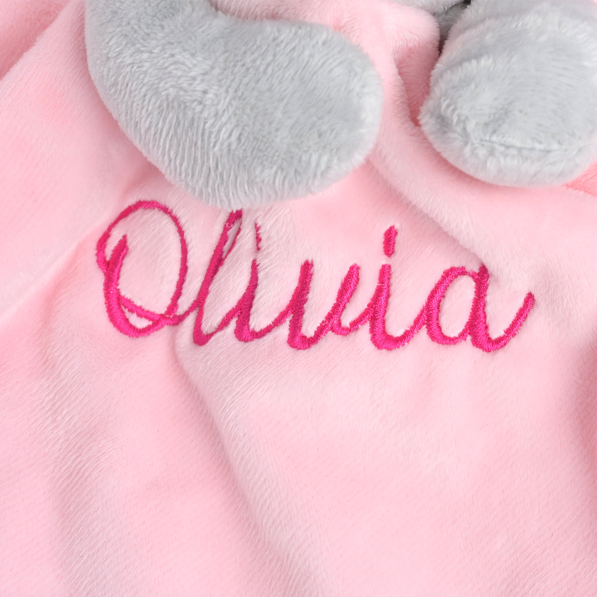 Close-up of a pink plush blanket with gray elephant ears and bright pink embroidered name 'Olivia'.