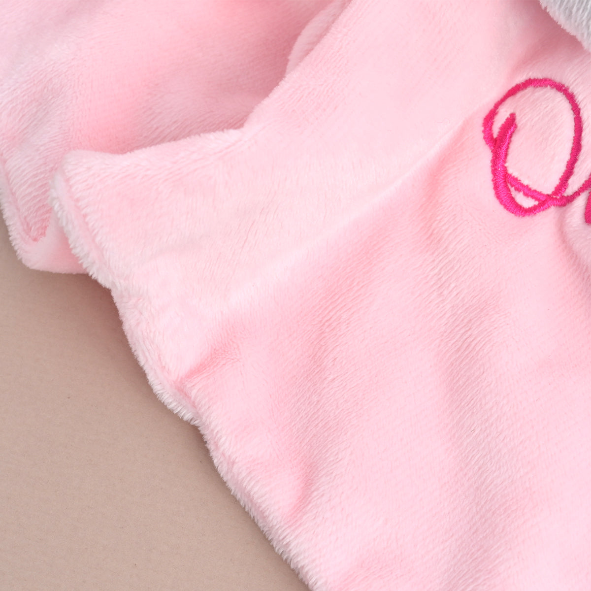 A close-up of a soft pink plush fabric, likely a blanket or quilt, featuring a bright pink embroidered letter 'Q' on a beige surface.