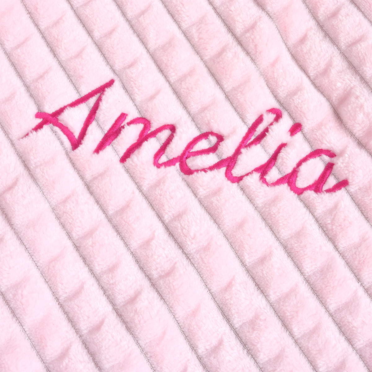 Close-up of the name Amelia embroidered in magenta thread on pink ribbed fleece, shown from a different angle.