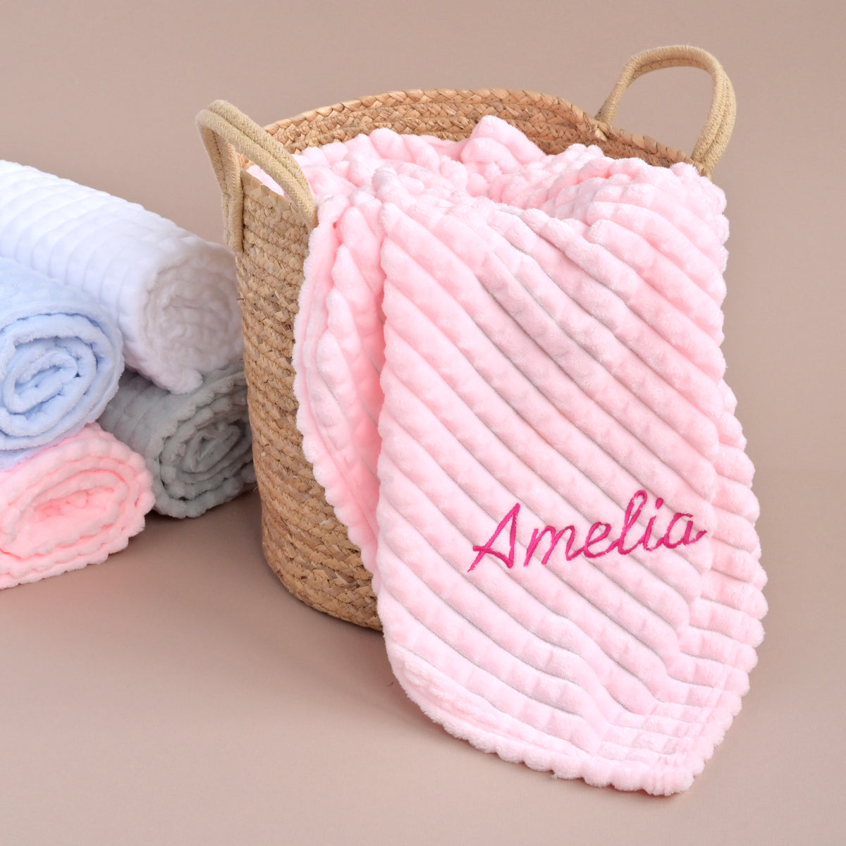 Pink ribbed fleece baby blanket personalised with the name Amelia, folded in a wicker basket.