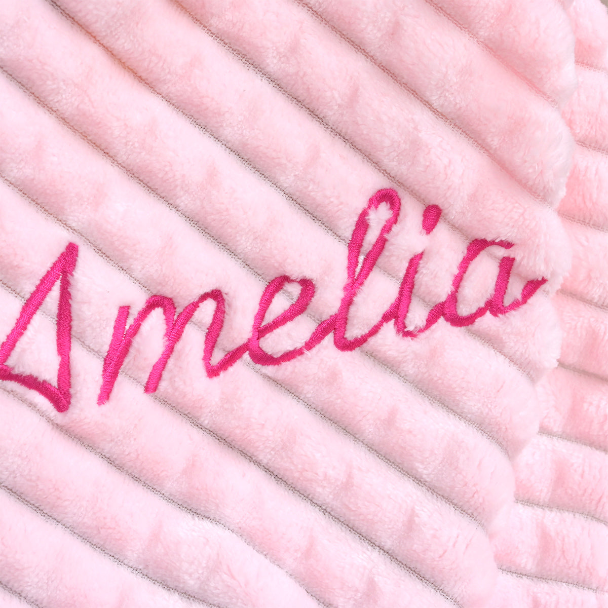 Close-up of the name Amelia embroidered in pink thread on ribbed fleece fabric, shown at an angle.