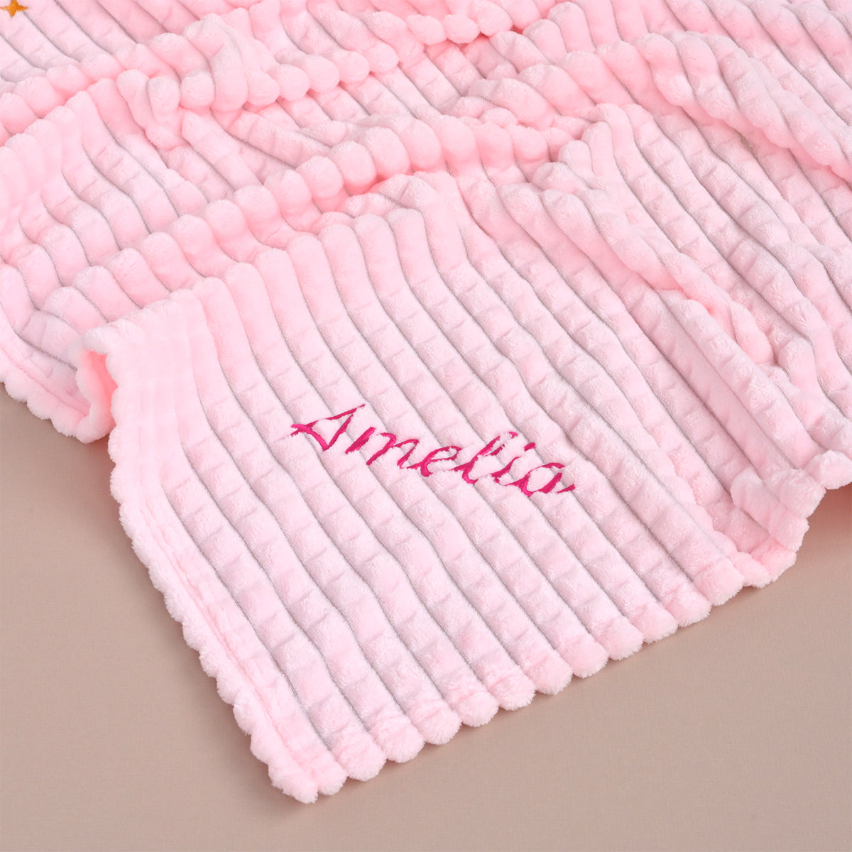 Pink ribbed fleece baby blanket folded flat, showing the name Amelia embroidered in magenta thread.