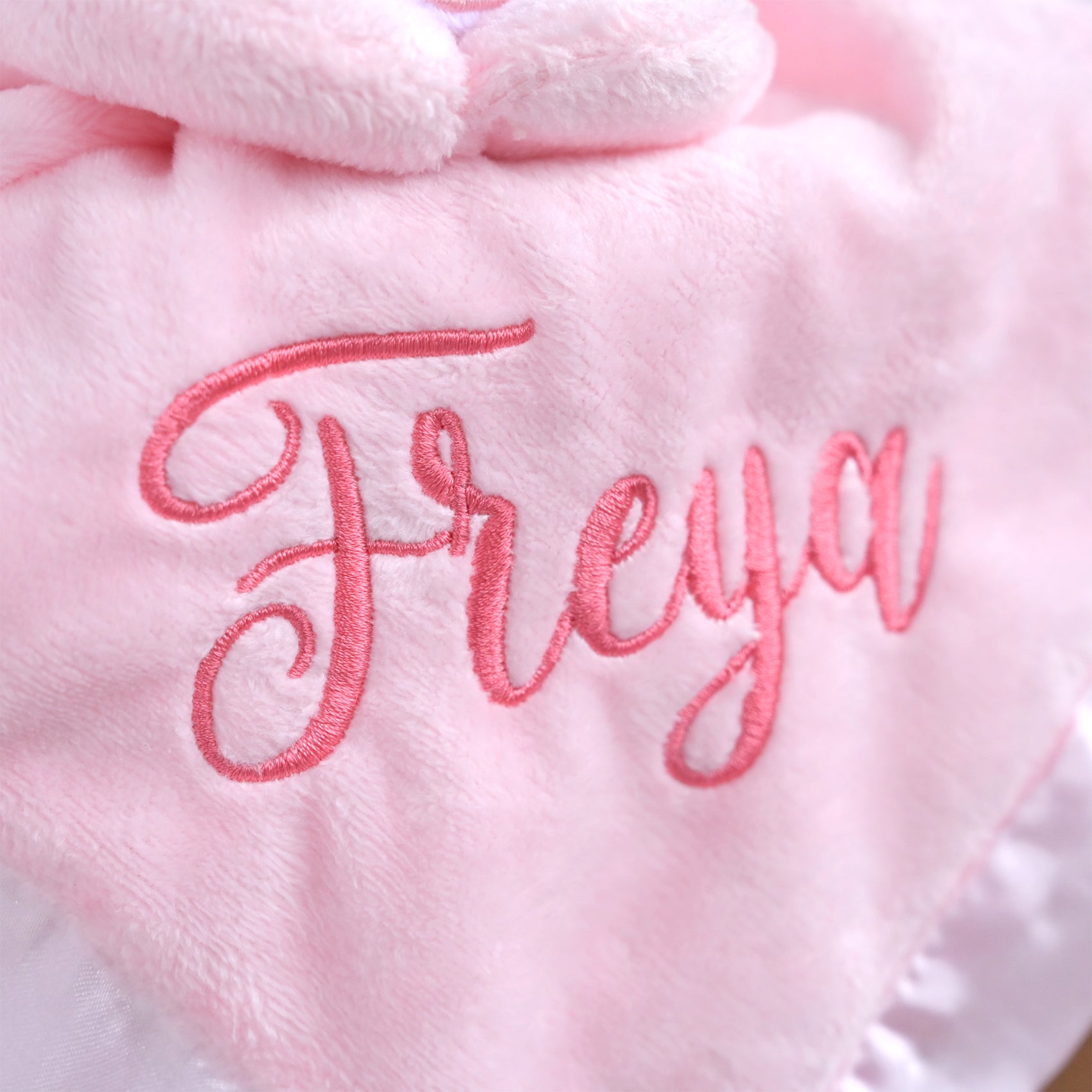 Close-up of a soft pink plush blanket or baby item with the name 'Freya' embroidered in pink script across the front.
