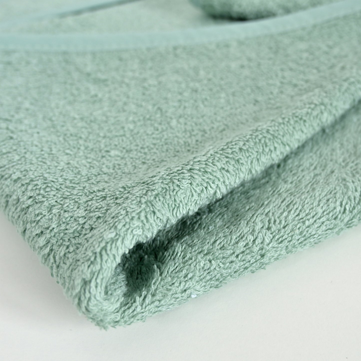 A close-up of a folded mint green terry cloth towel showing its soft, textured surface on a plain white background.